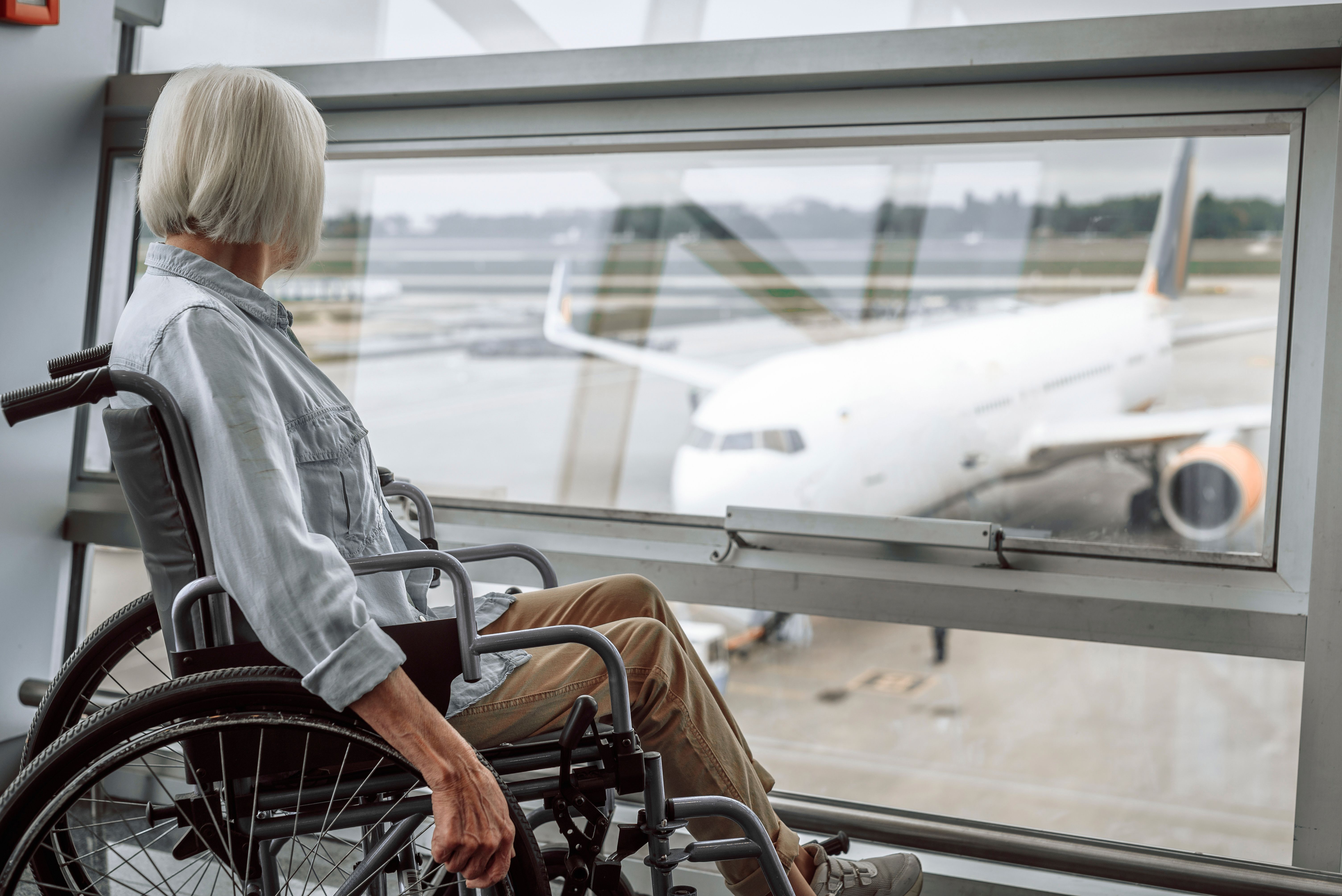 shutterstock_1424469368 - elderly lady in wheelchair waiting for generic jetliner at airport