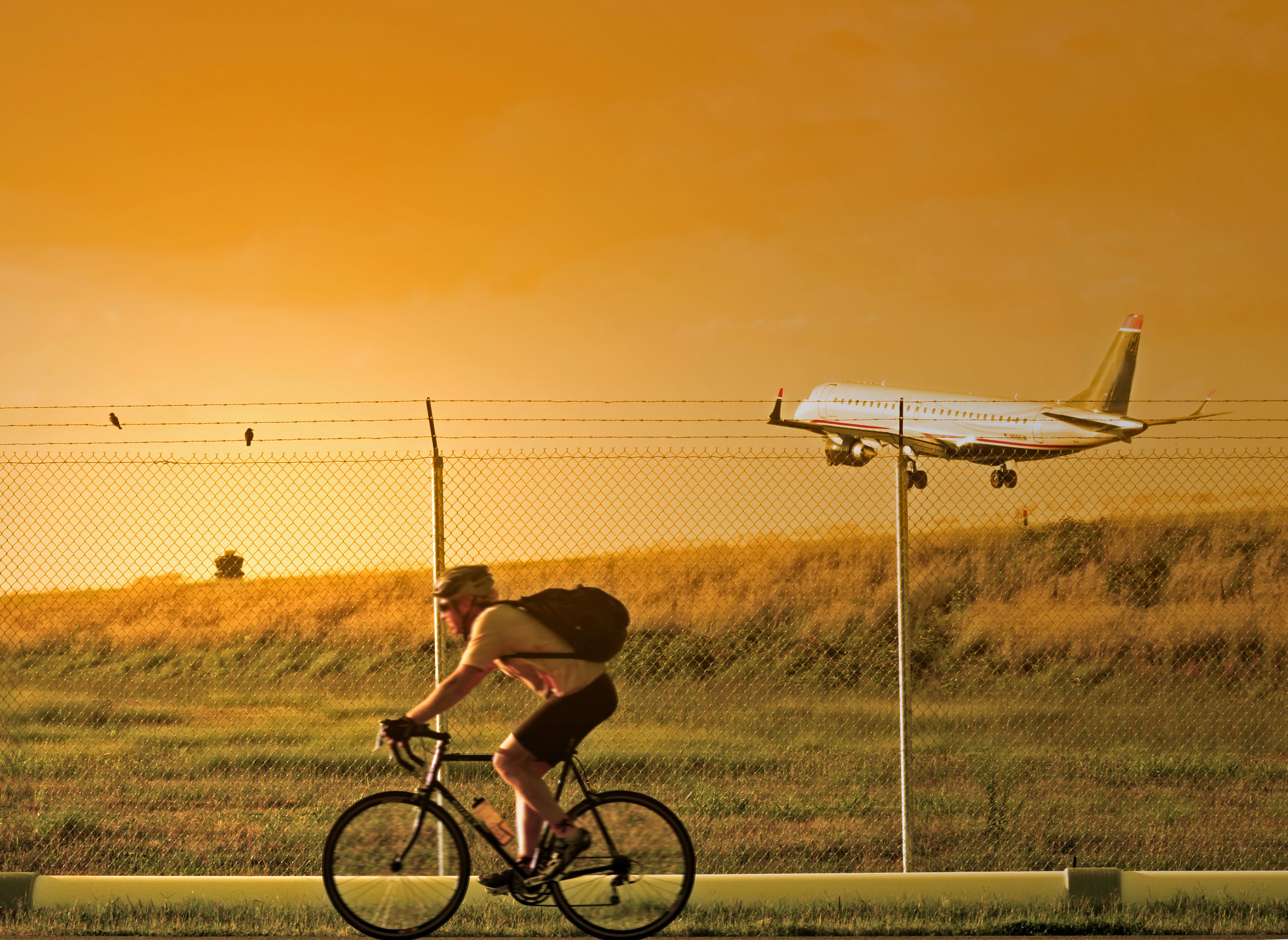 Someone riding a bike near an airport as an aircraft comes in to land.