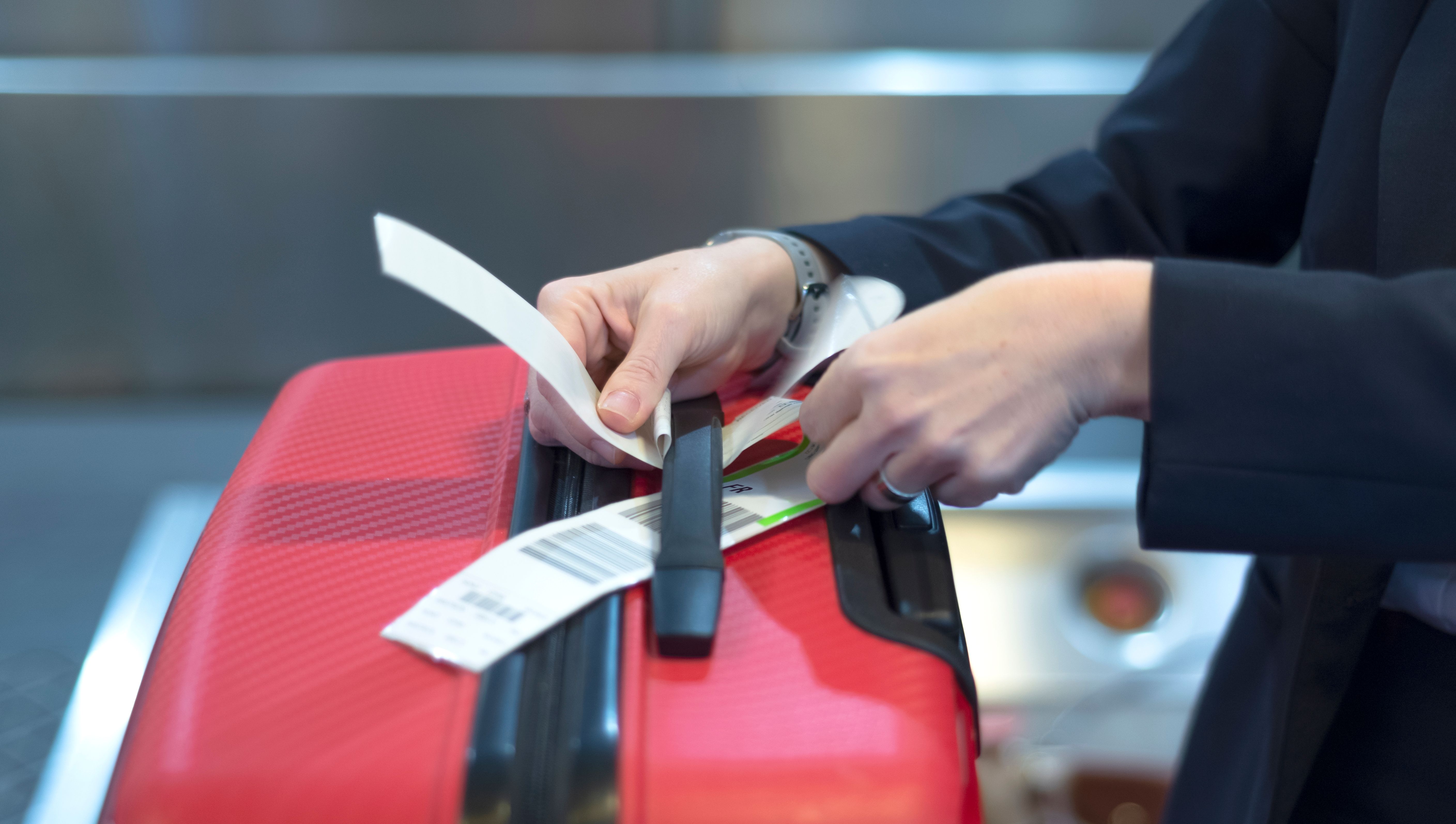 A check-in employee attaching a luggage tag to a suitcase.