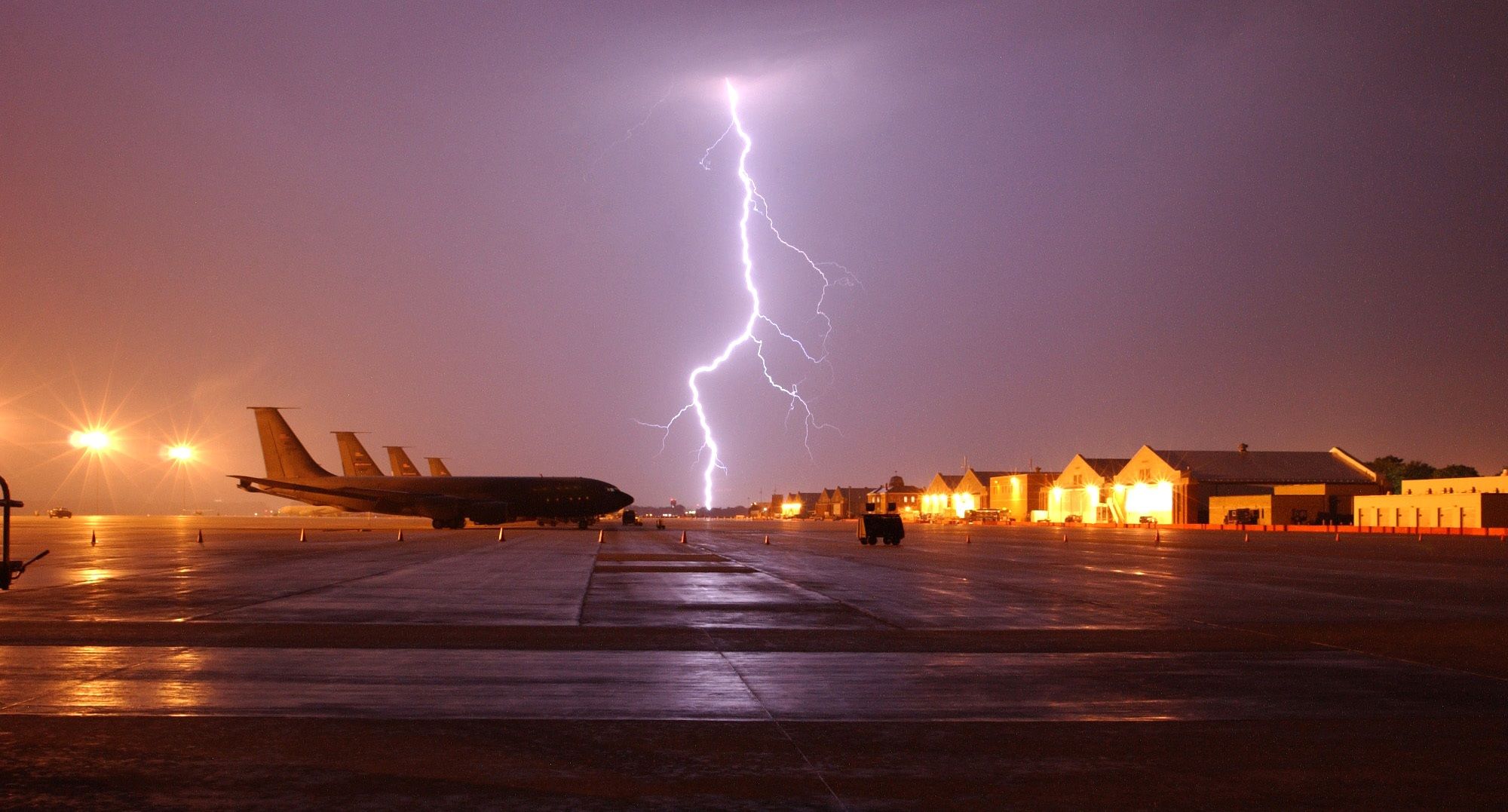 many aircraft lined up at an airfield during a thunderstorm.