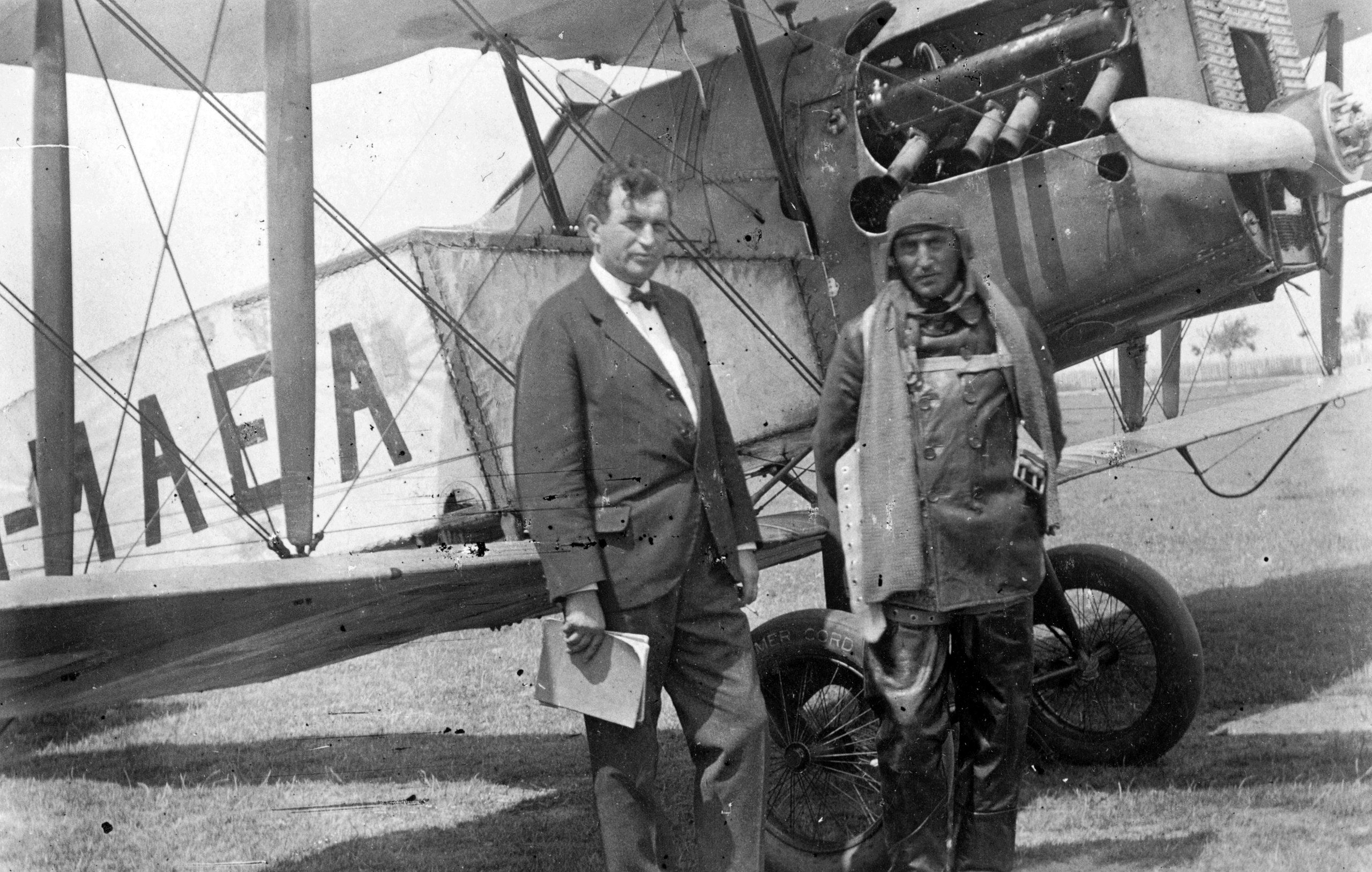 Two men, one with aviator gear and the other wearing a suit, standing in front of a Bristol F28.