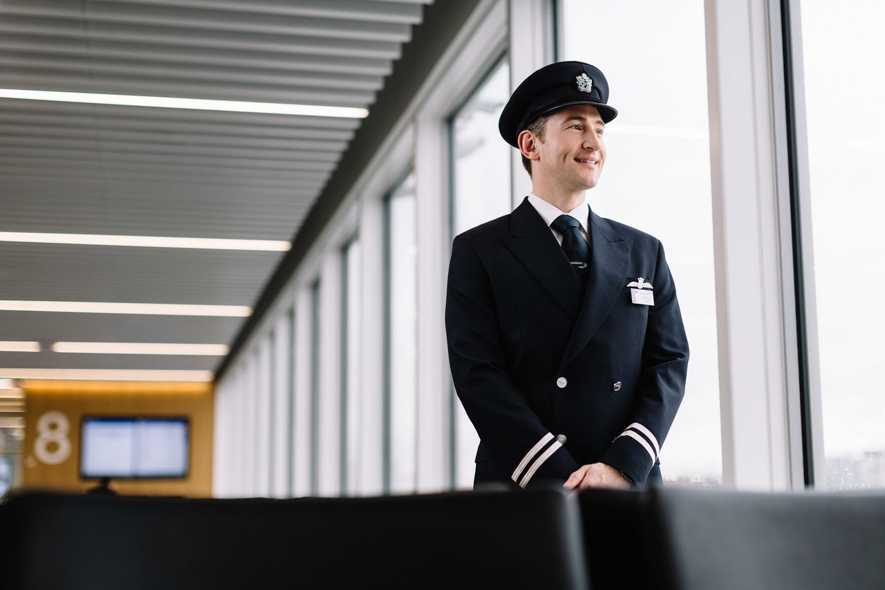 A British Airways Pilot in uniform standing near an airport terminal window.