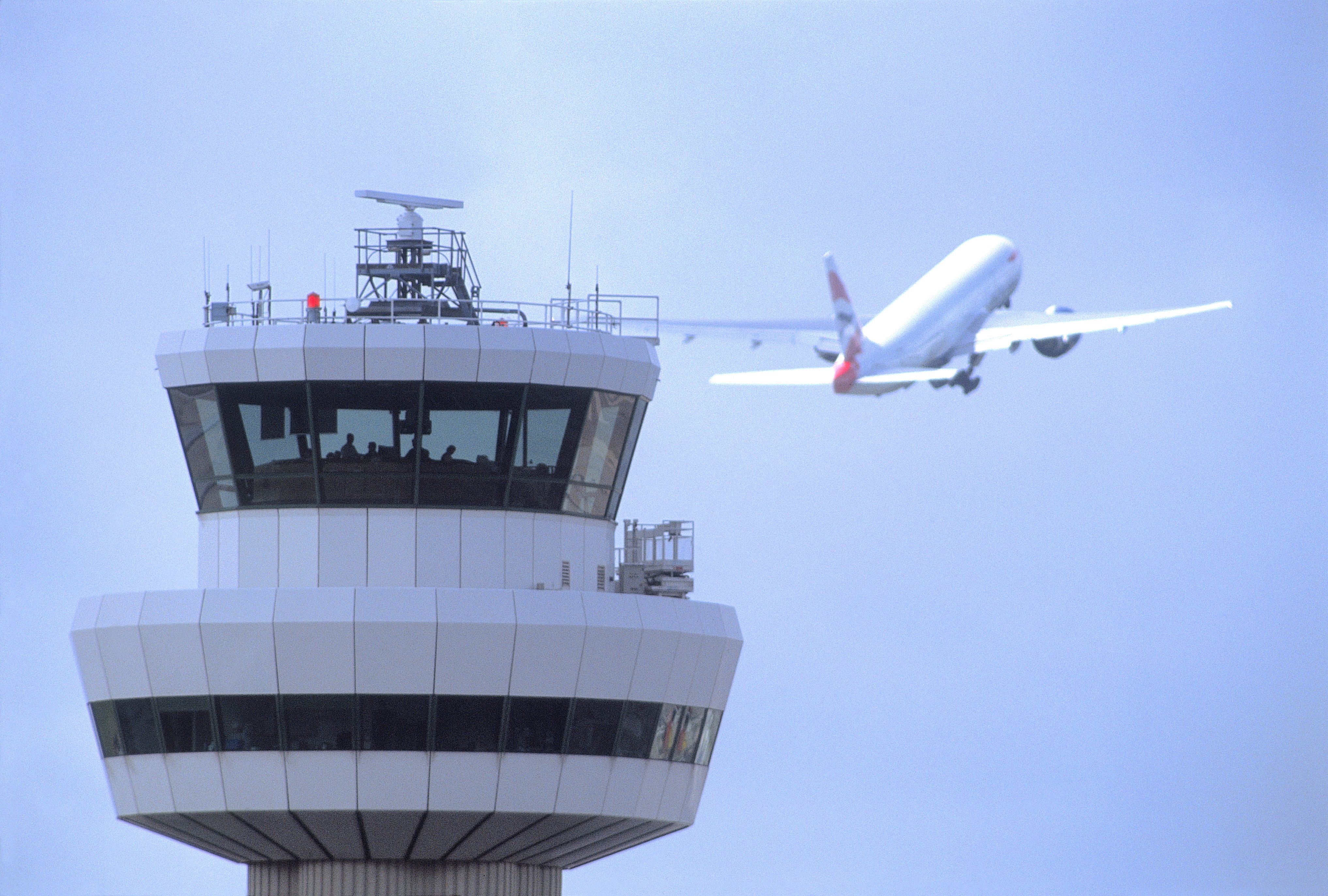 A British Airways Aircraft flying behind London Gatwick Airport's ATC Control Tower.