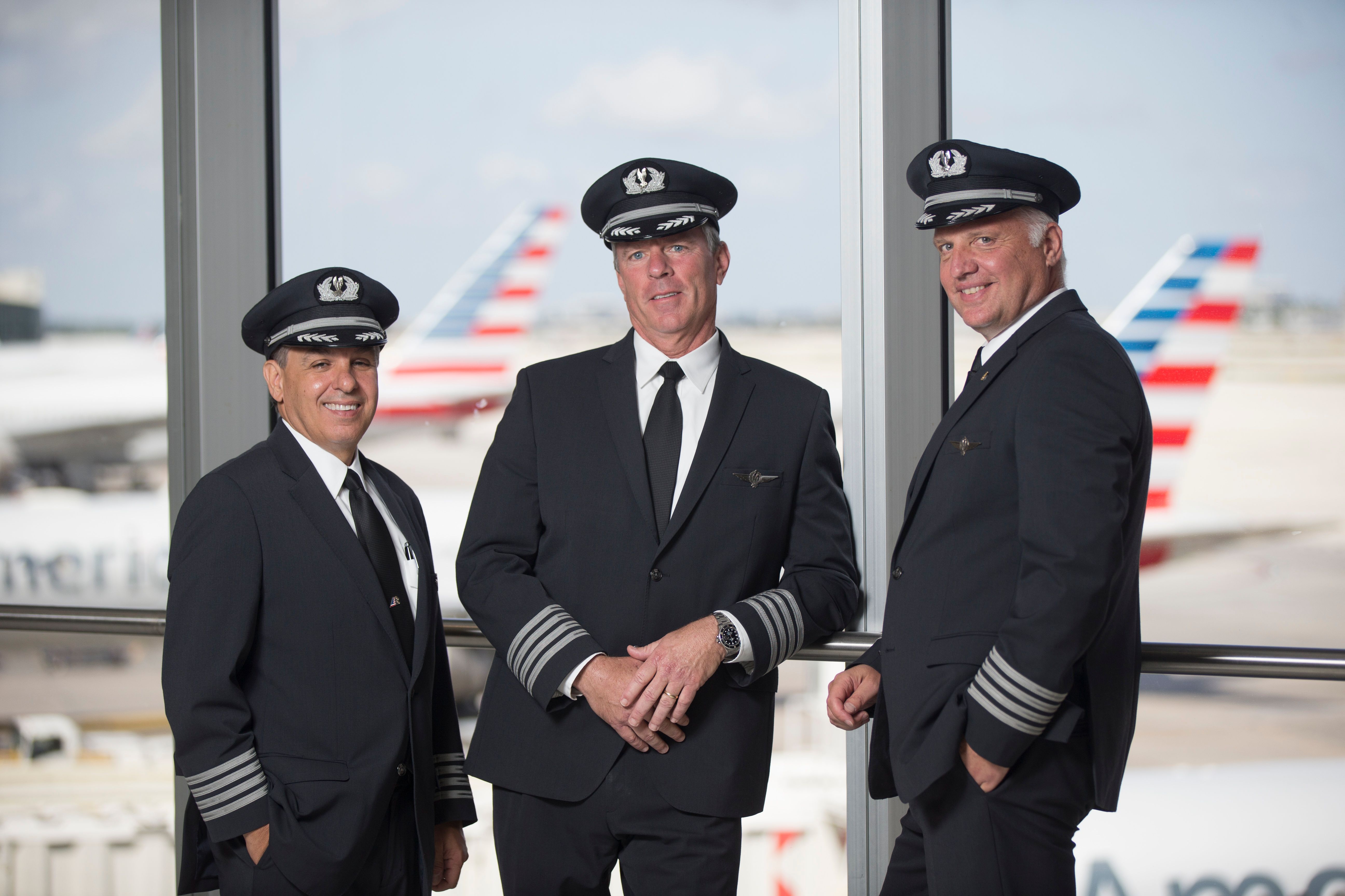 Three American Airlines captains standing near an airport terminal window.