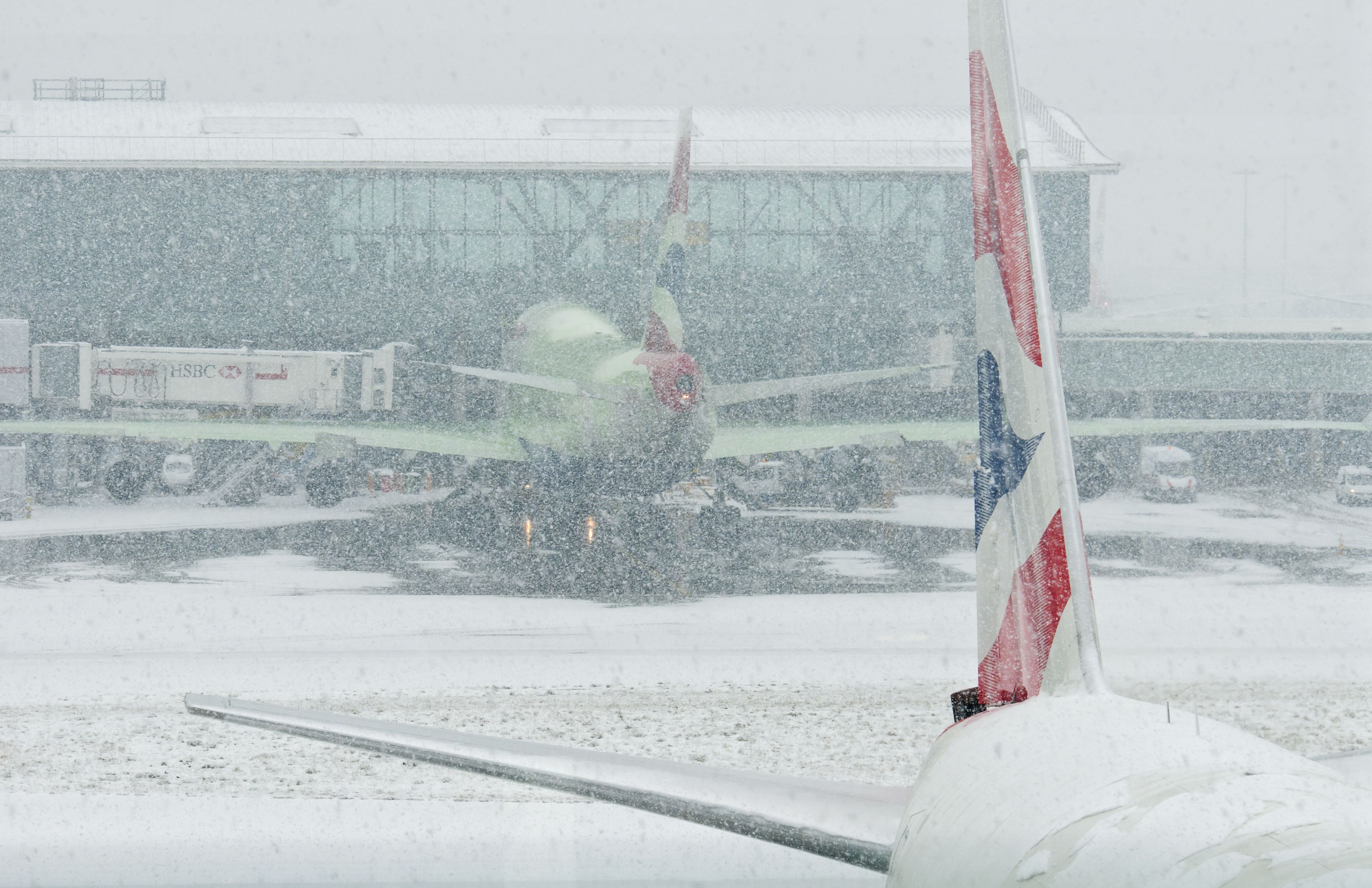 Two British Airways aircraft parked at London Heathrow on a snowy day.