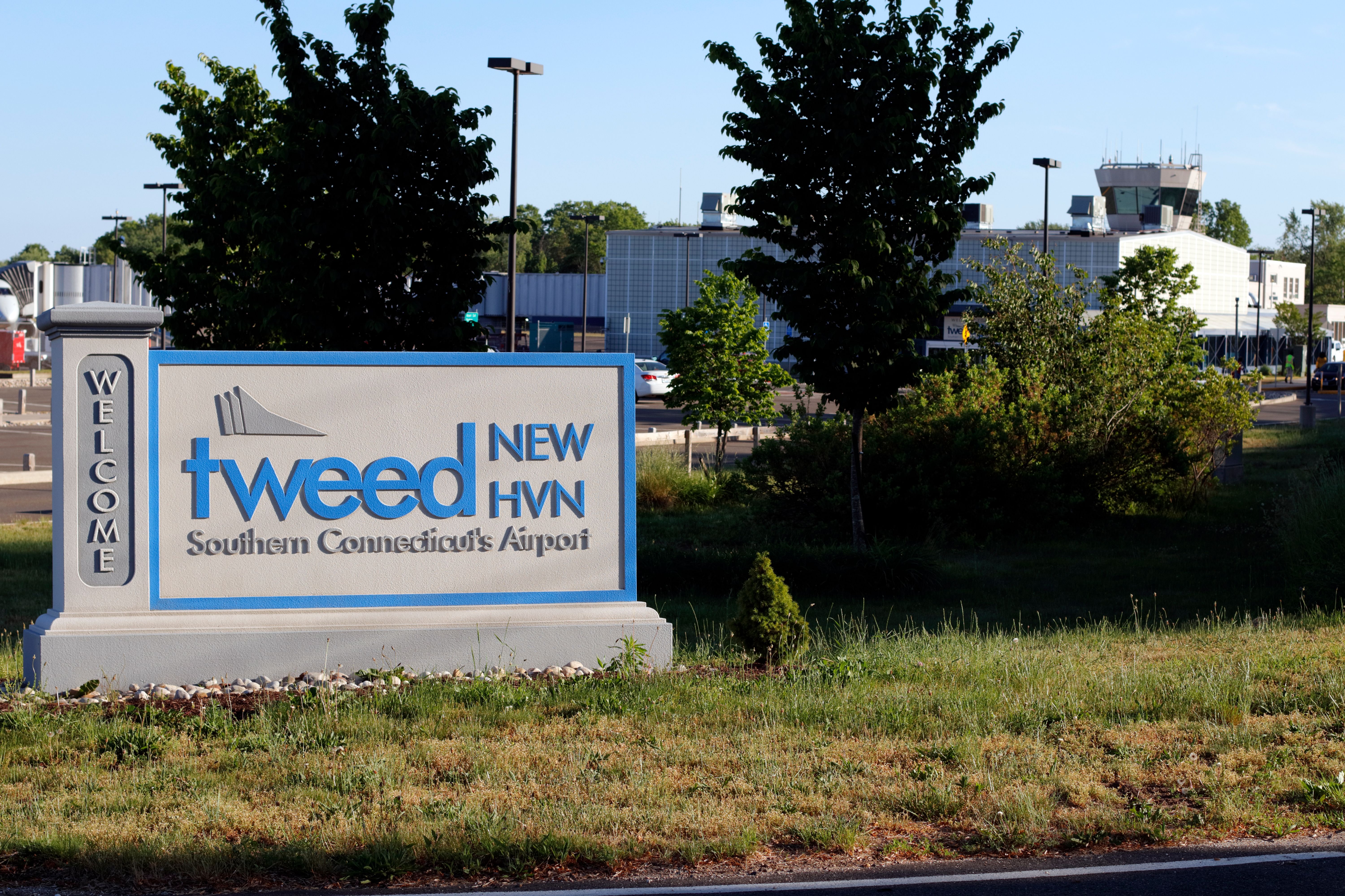 Entrance sign to Tweed New Haven Airport on a sunny evening with airport in back.