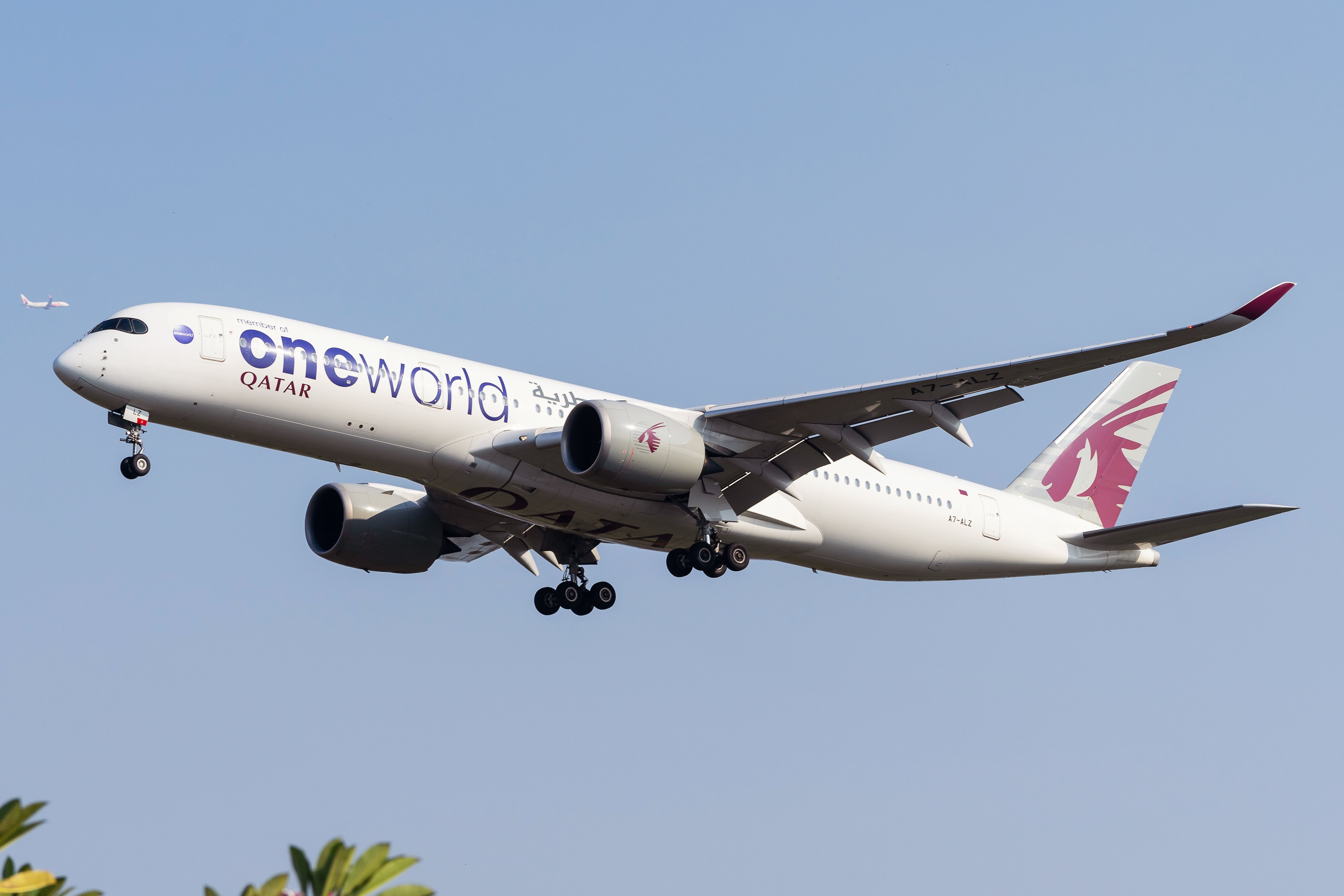 A Qatar Airways Airbus A350 in oneworld livery flying in the sky.
