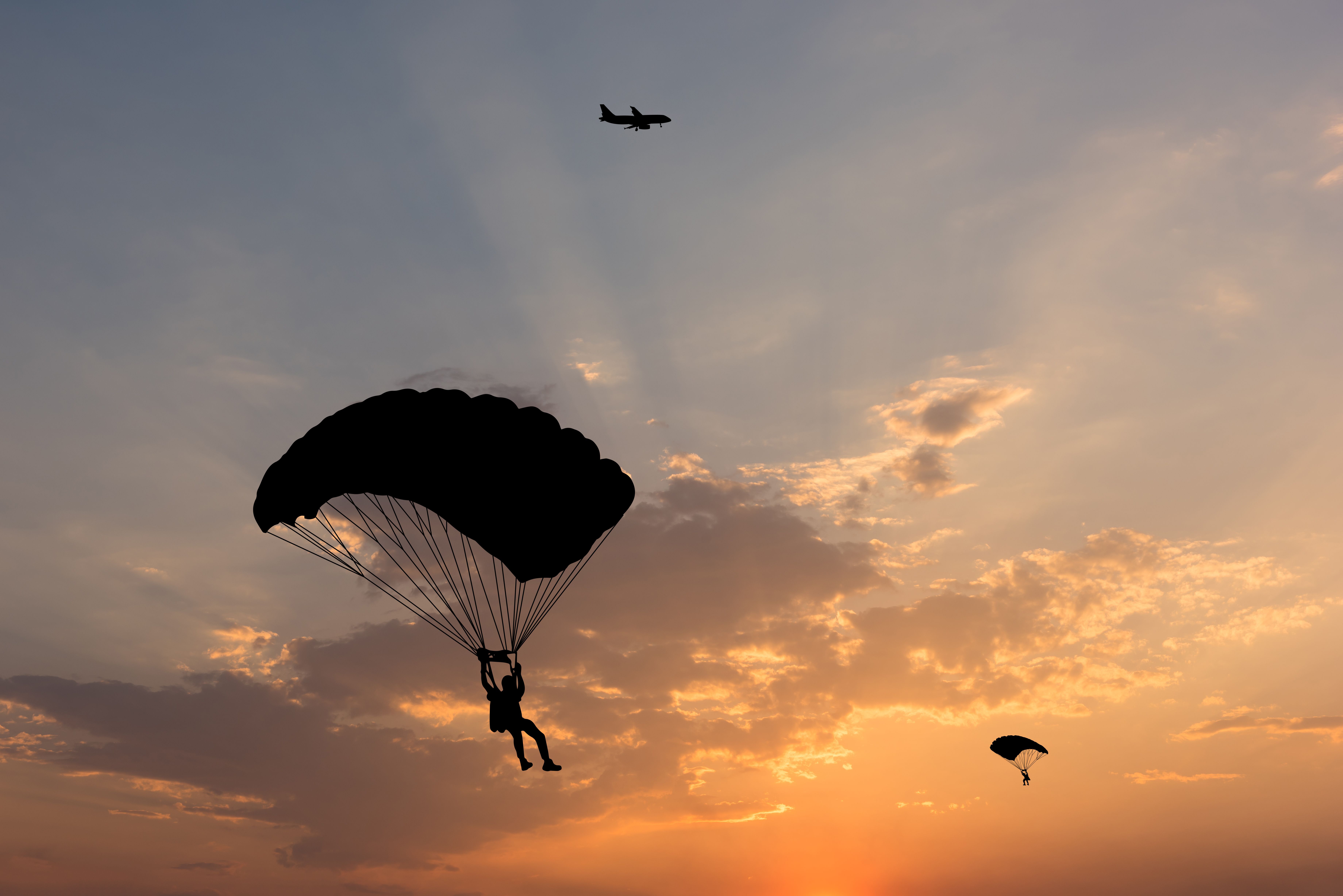 Two divers using parachutes as an aircraft flies overhead.