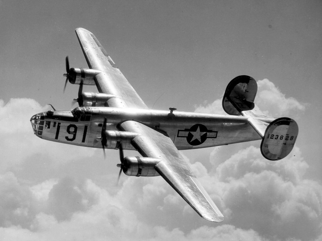 A Consolidated B-24 Liberator glistens in the sun as it makes a turn in the clouds.