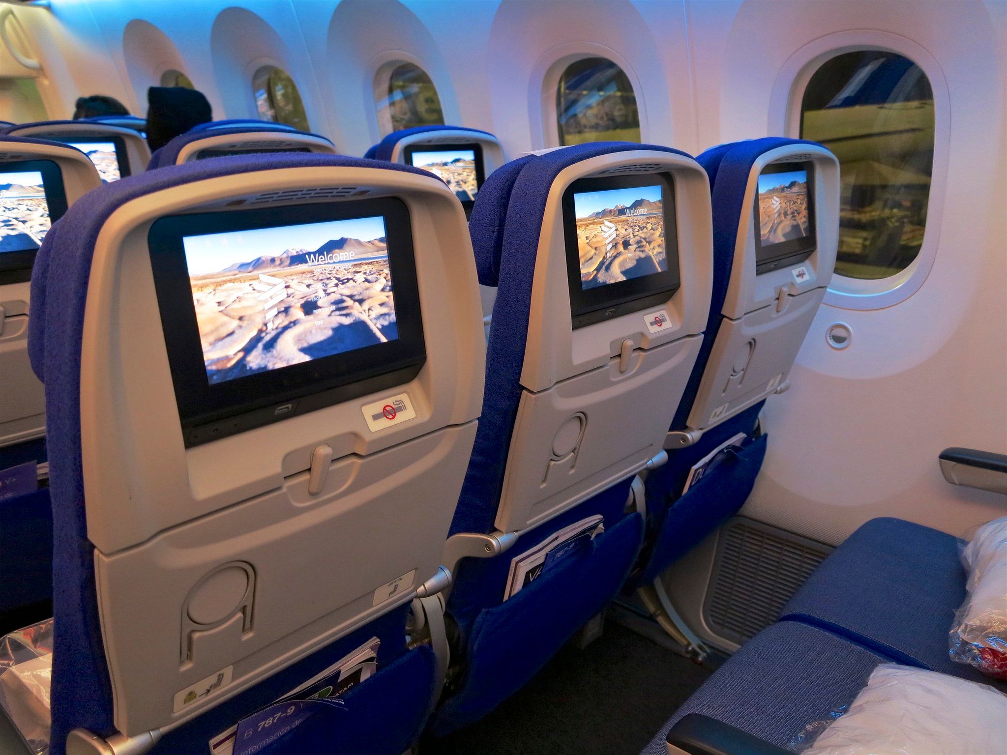 Inside an economy class cabin, focusing on the inflight entertainment screens behind each seat.