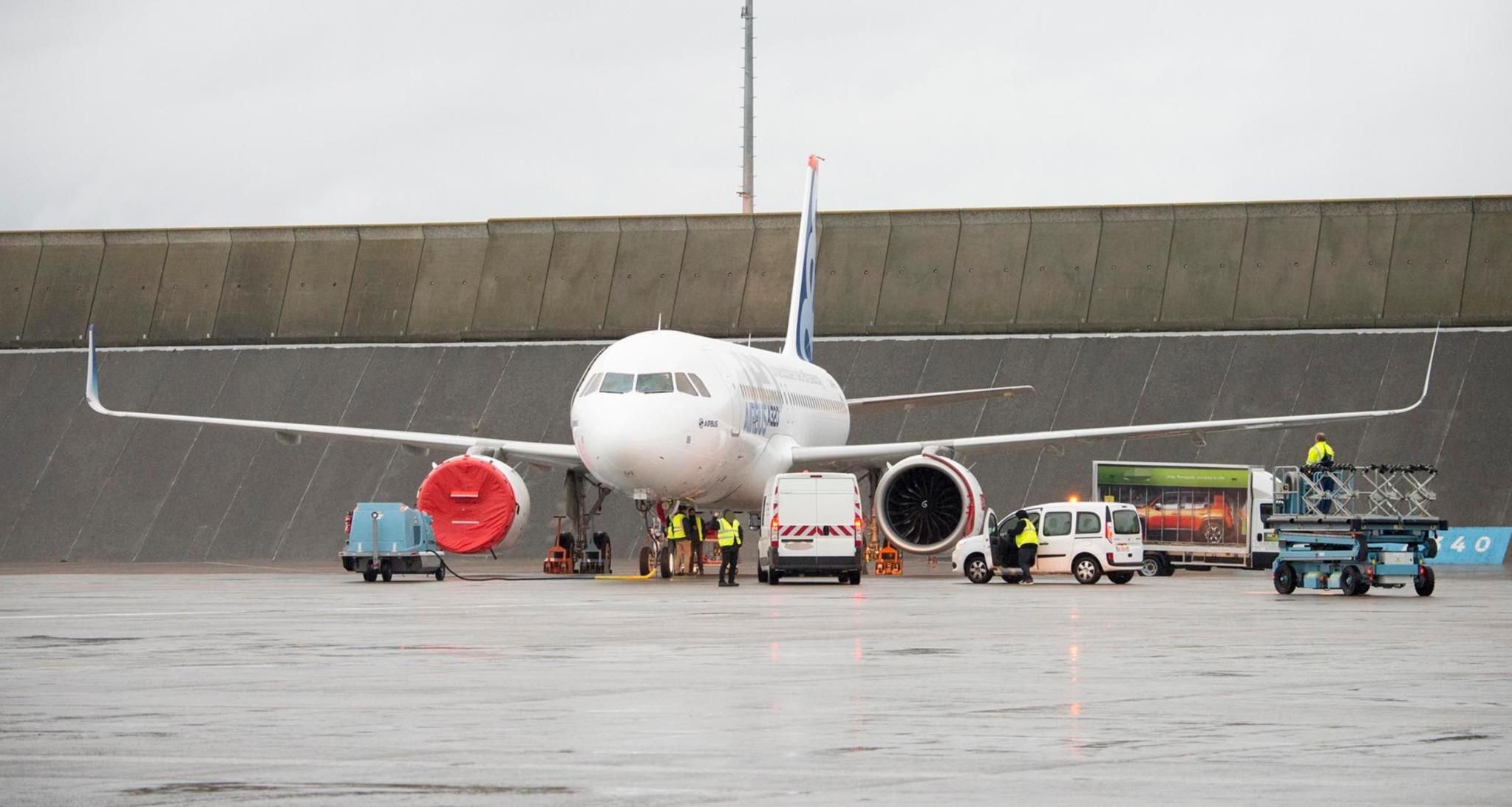 A parked aircraft, with workers putting on engine covers.
