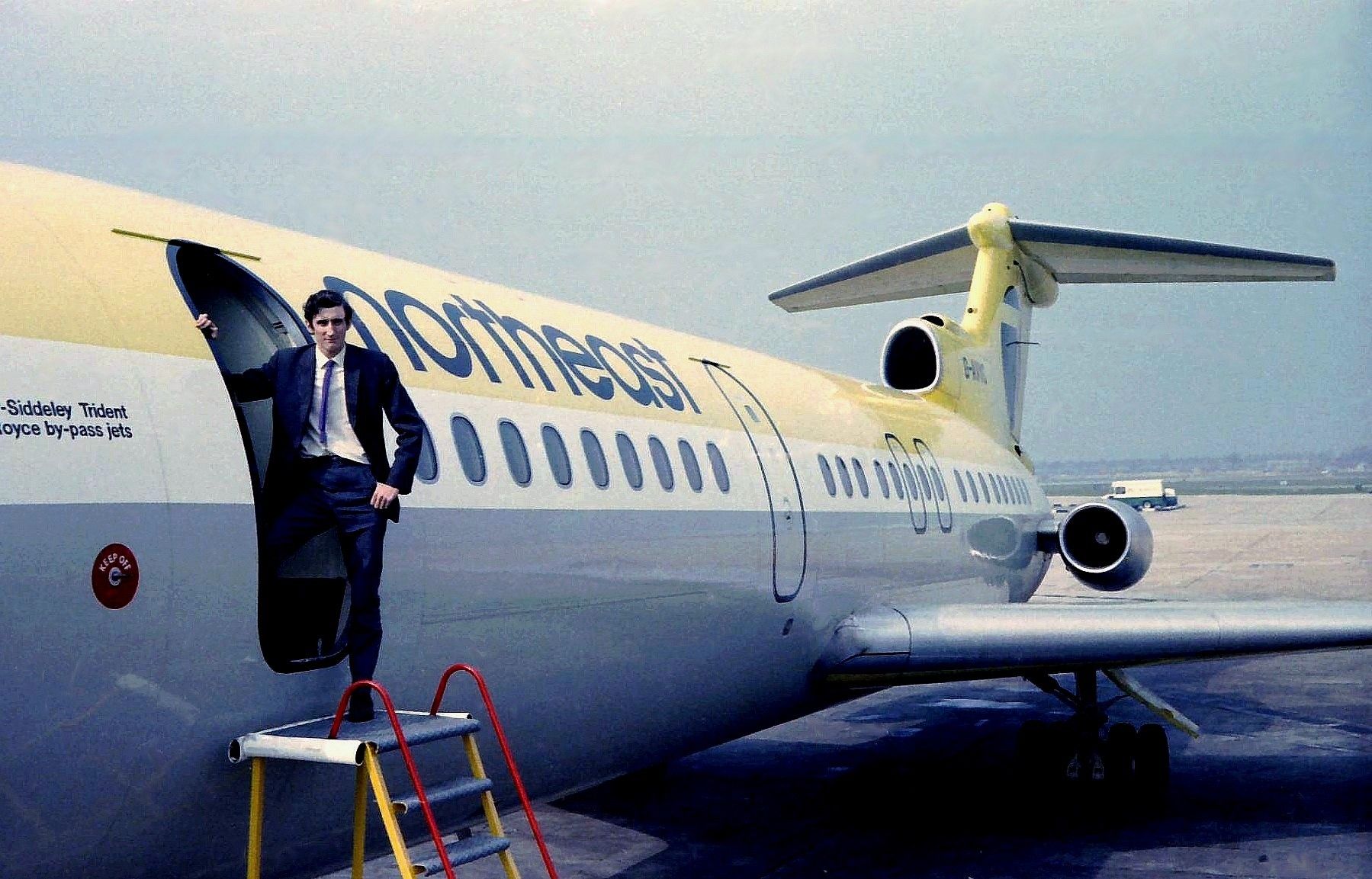 A flight attendant standing in the doorway of a Northeast Airlines Trident aircraft.