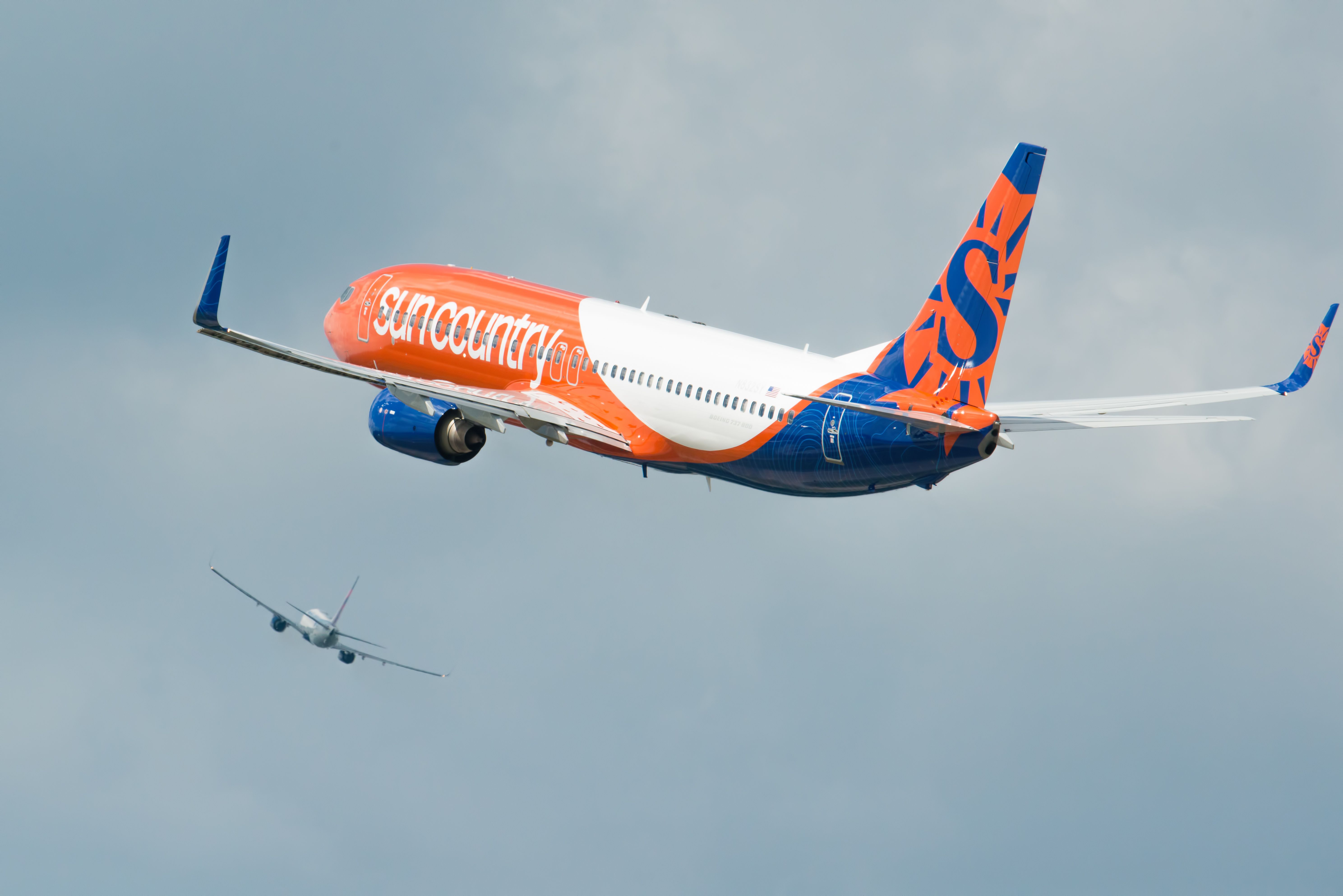A Sun Country Airlines aircraft flying just just behind another aircraft in the distance.