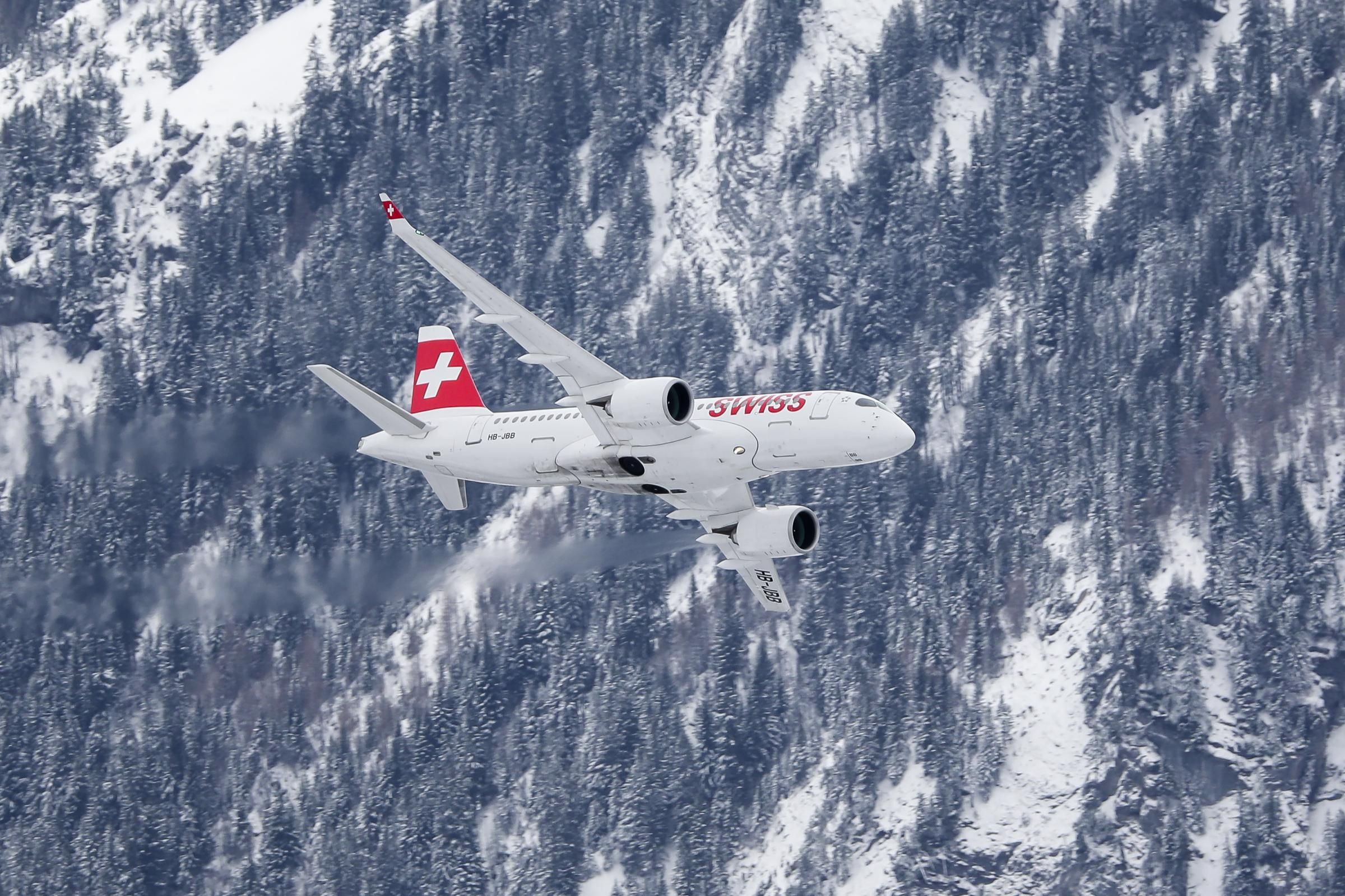 A SWISS Airbus A220 flying near a mountain.