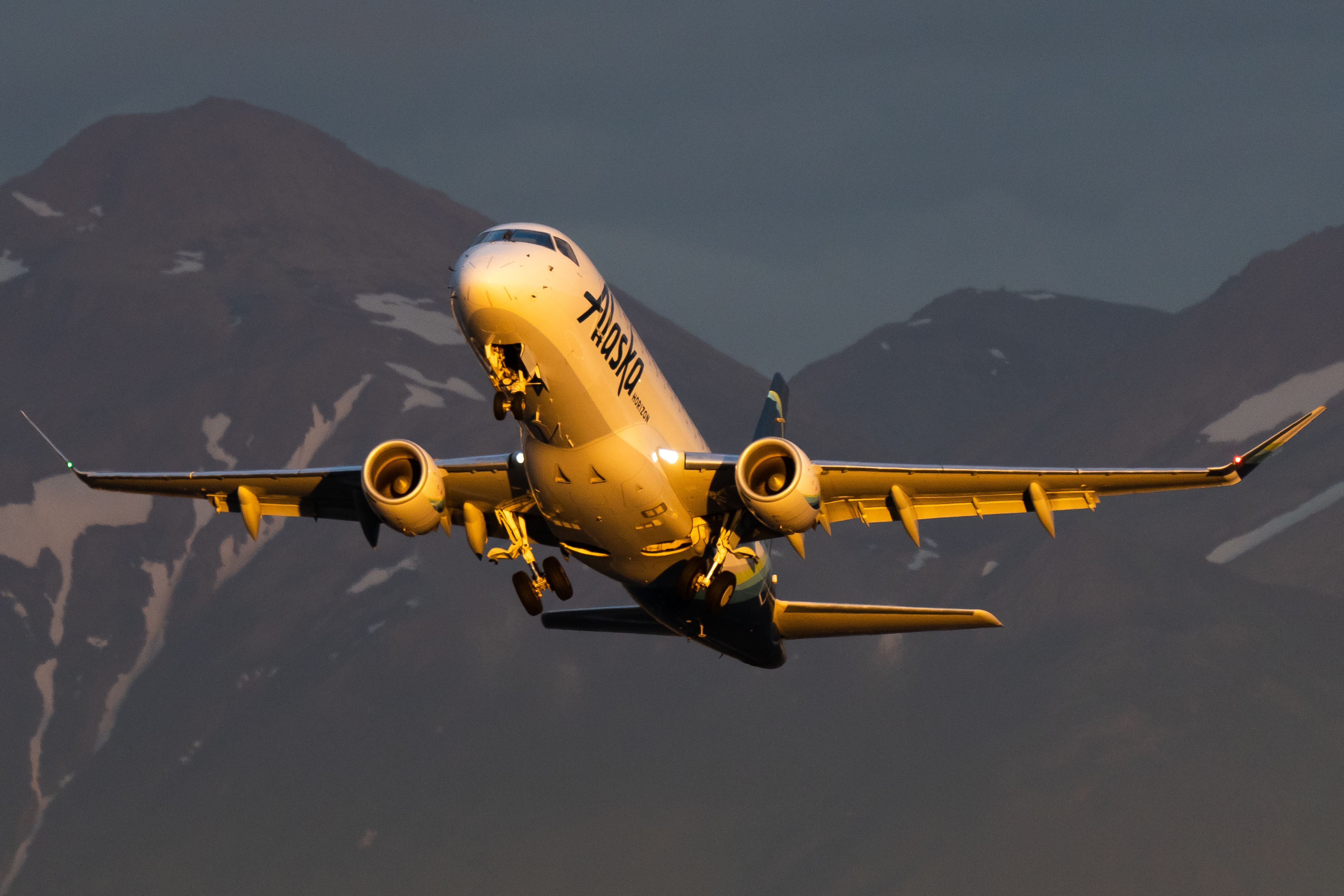 An Alaska Airlines Boeing 737-790 climbing with mountains in the background.