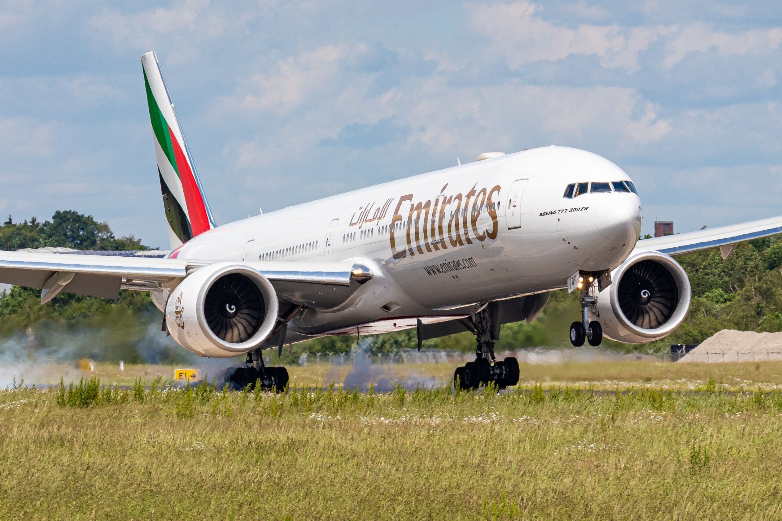 An Emirates 777-300ER just as it lands on a runway.