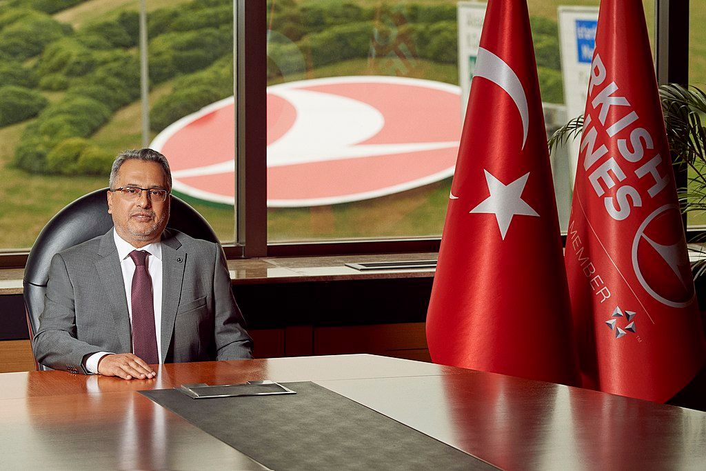 A Turkish Airlines company leader sits at an office table, near two Turkish Airline flags.