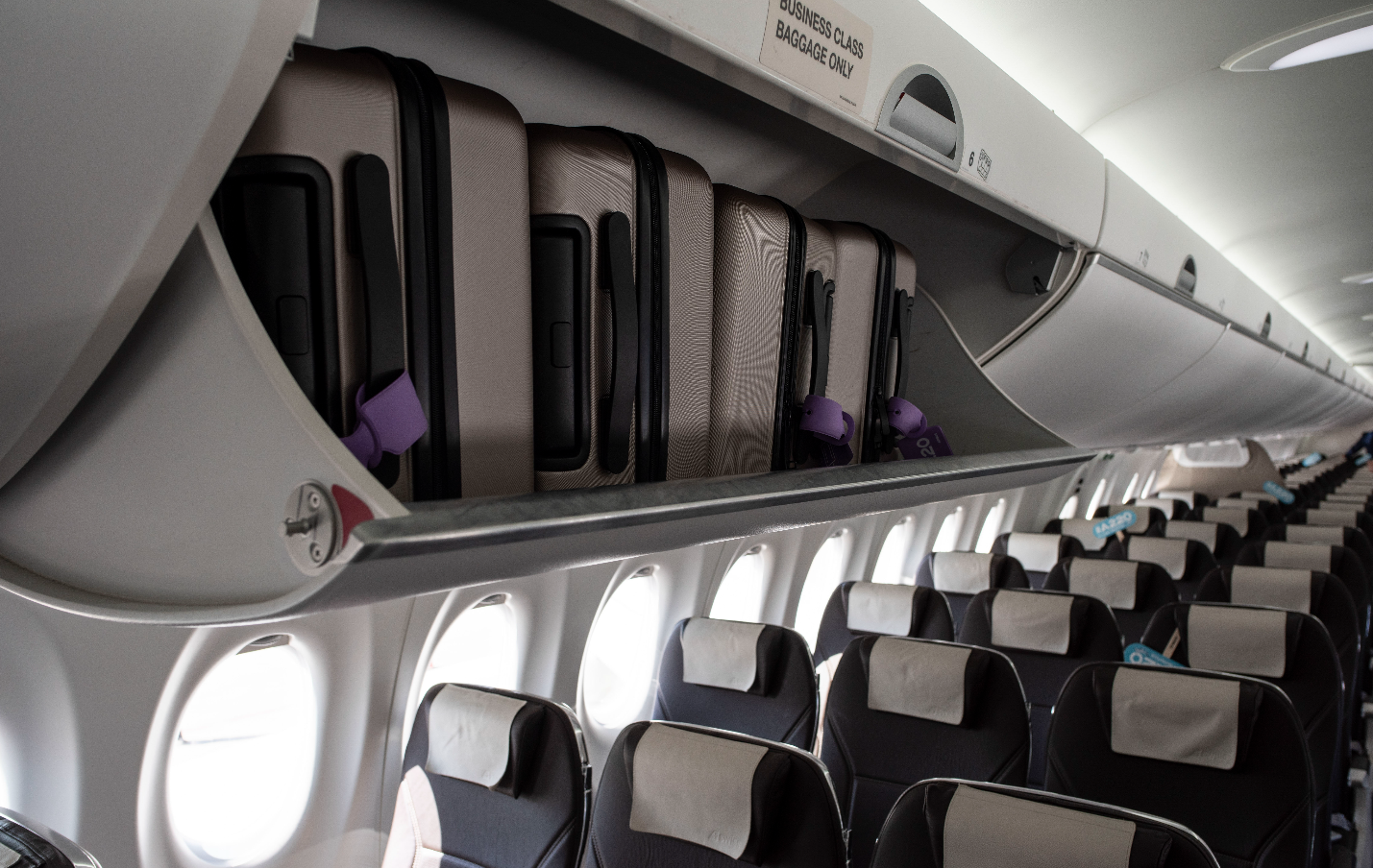 Inside the Airbus A220 cabin with storage bins open.