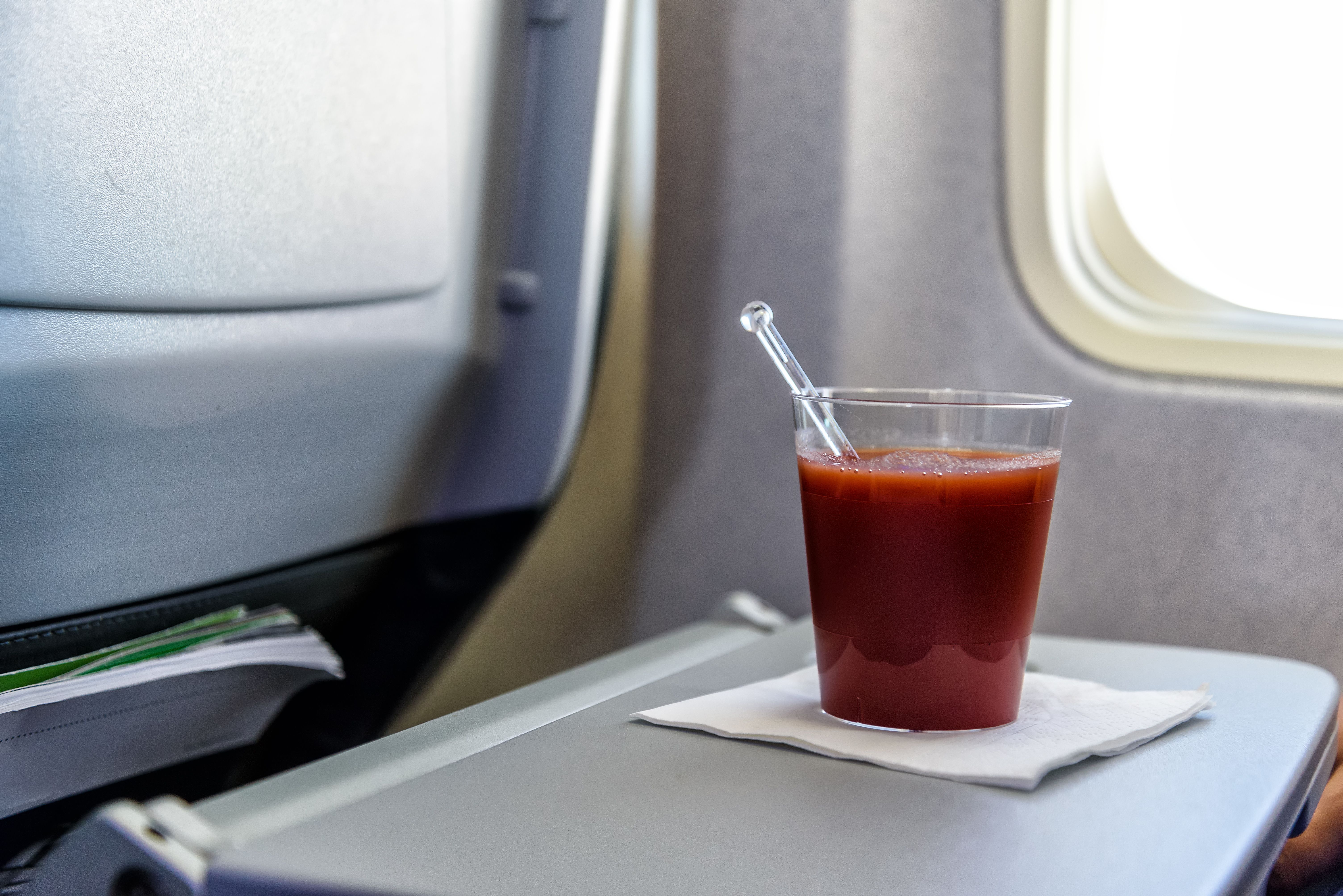 A glass of tomato juice on a seatback tray table.