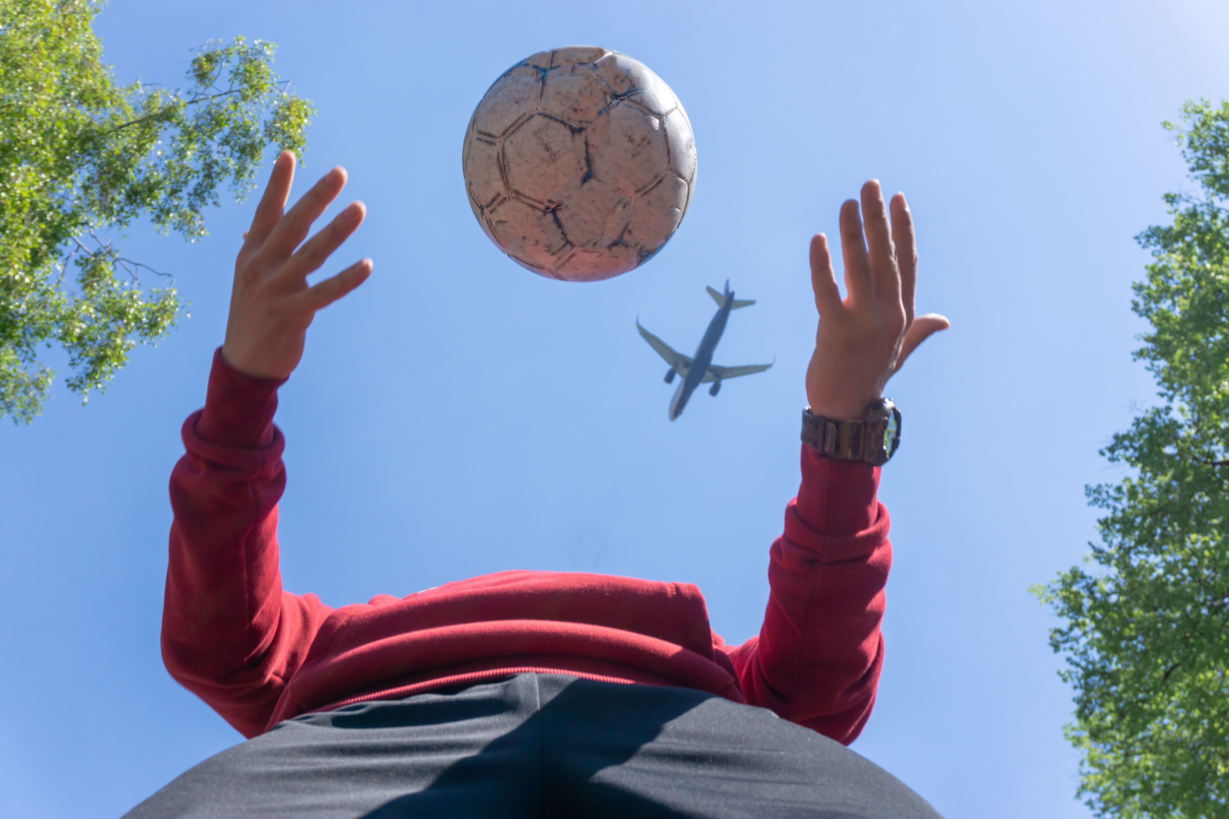someone using a football at a park as an aircraft travels overhead.
