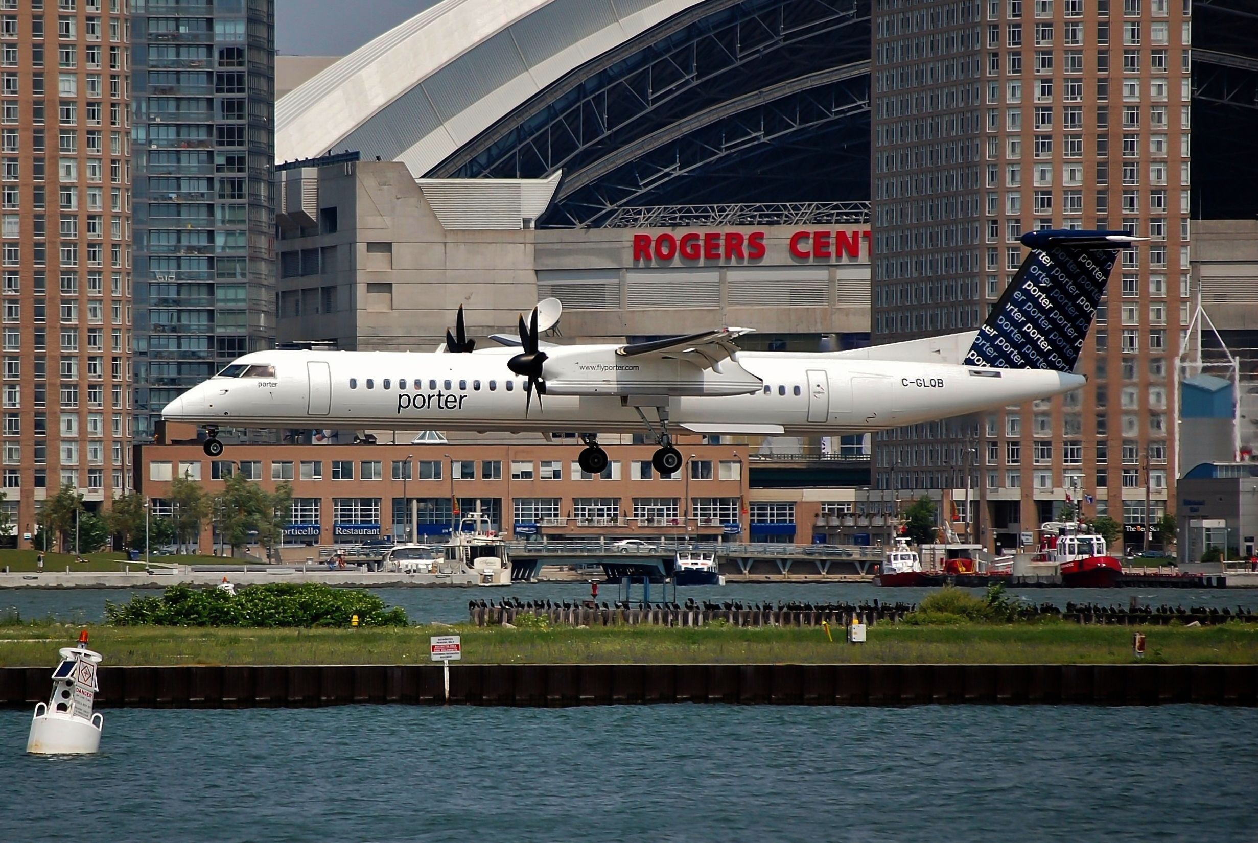 shutterstock_1489379777 - Porter Airlines Bombardier DHC-8-402 Q400, Registration C-GLQB landing at the Toronto Billy Bishop City (City Centre / Toronto Island airport in front of the Rogers Center. Toronto, Canada July 2 2011