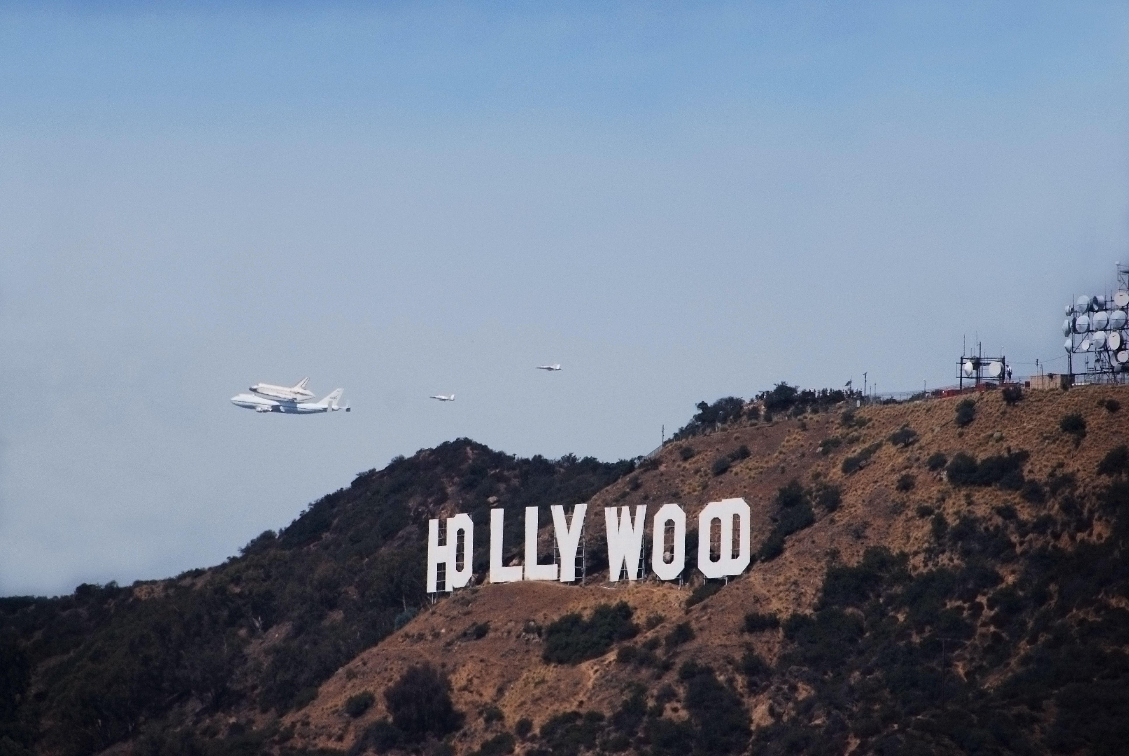 The famous Hollywood sign with a Boeing 747 carrying a space shuttle in the background.