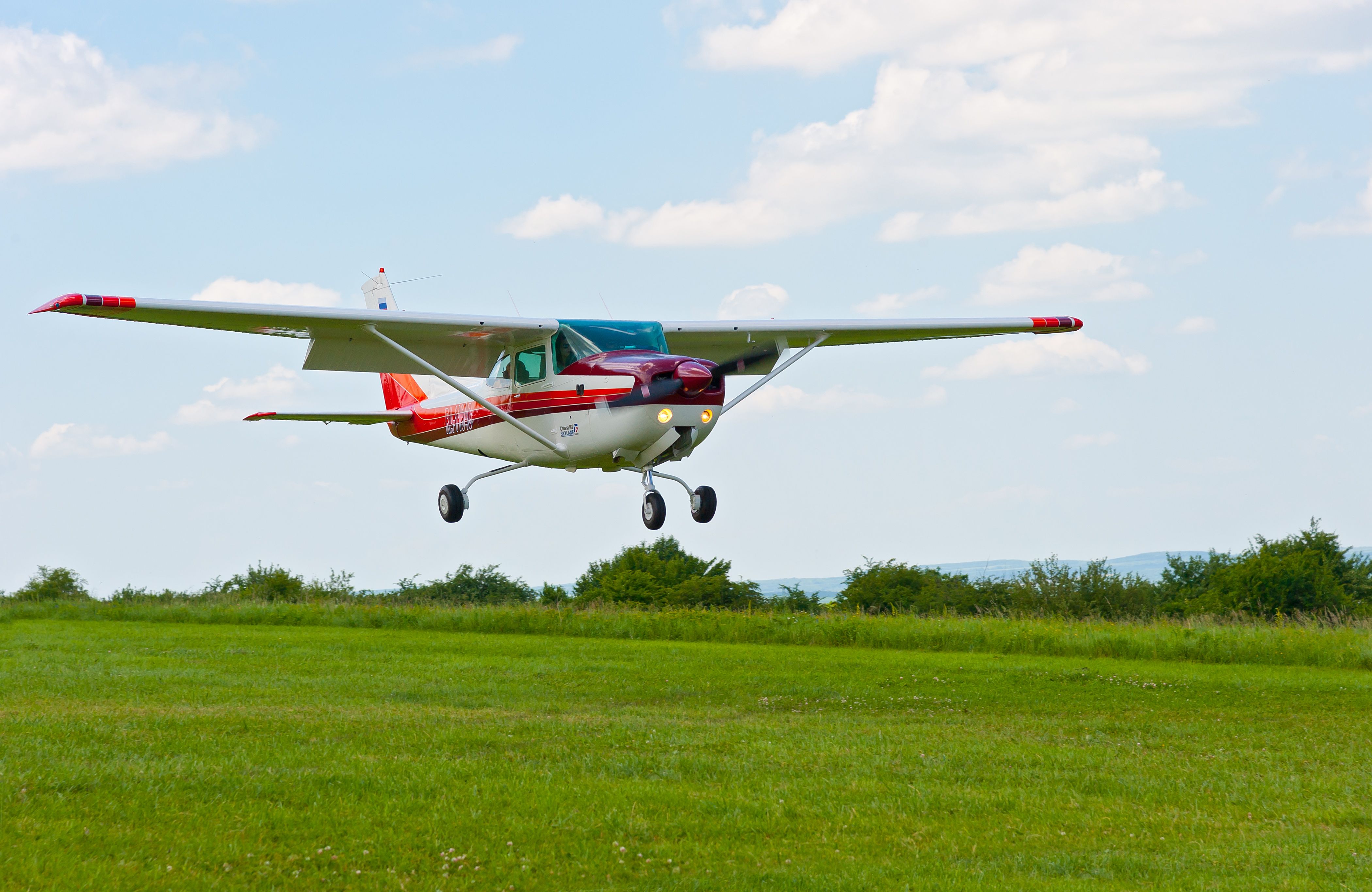 A private small aircraft landing on a grass runway. 