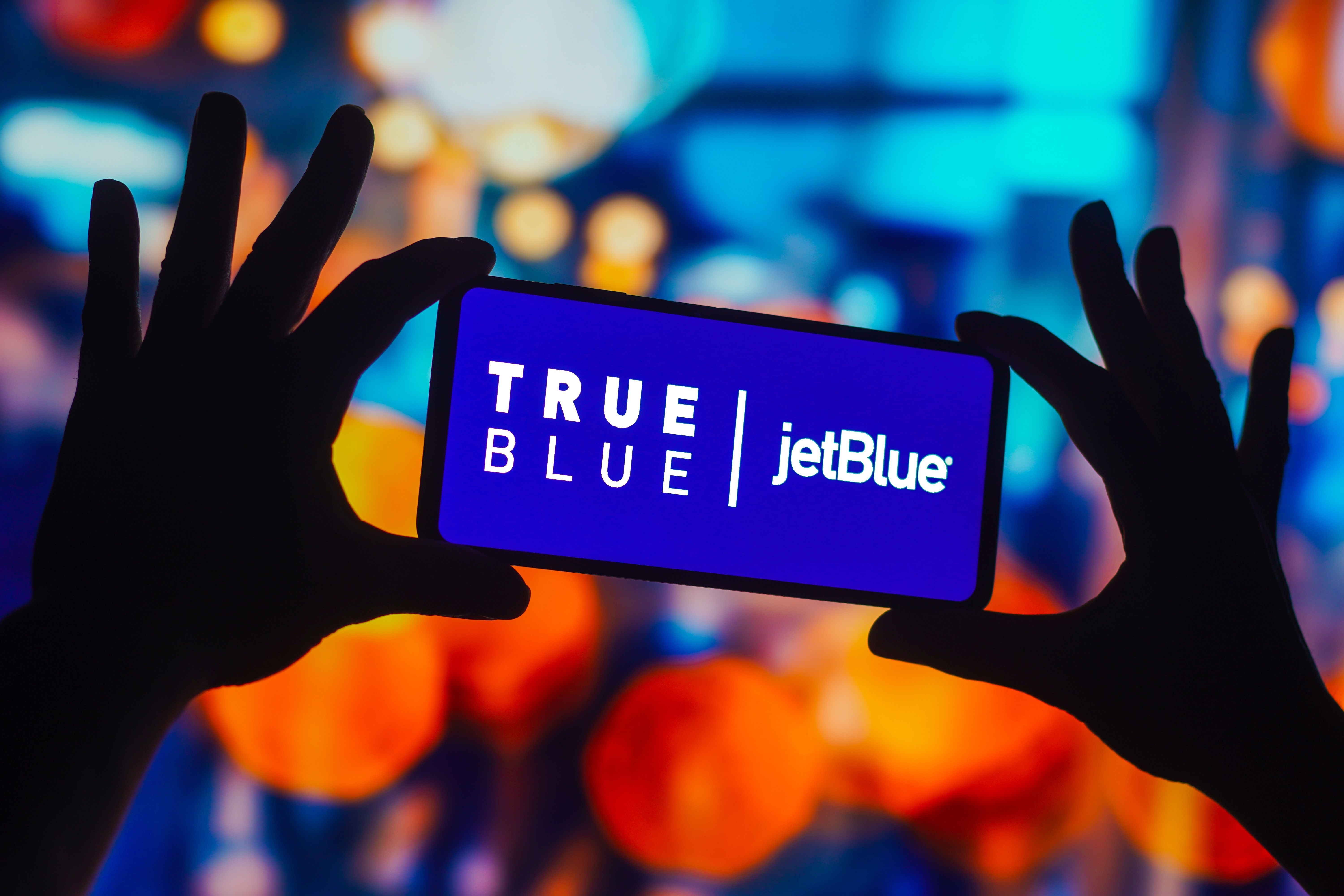 A person holding up a mobile device with the words JetBlue true blue written on it.