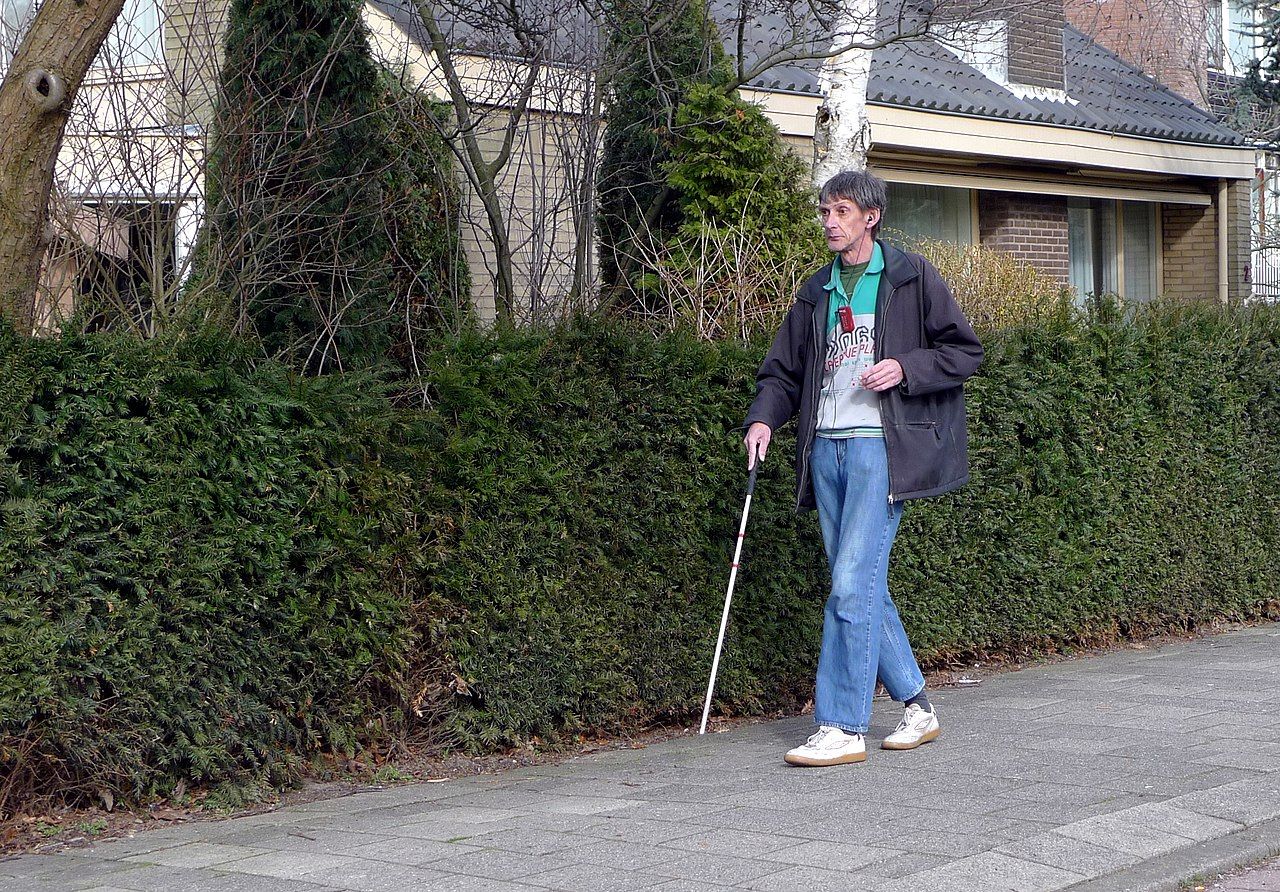 A visually impaired individal walking with a cane.