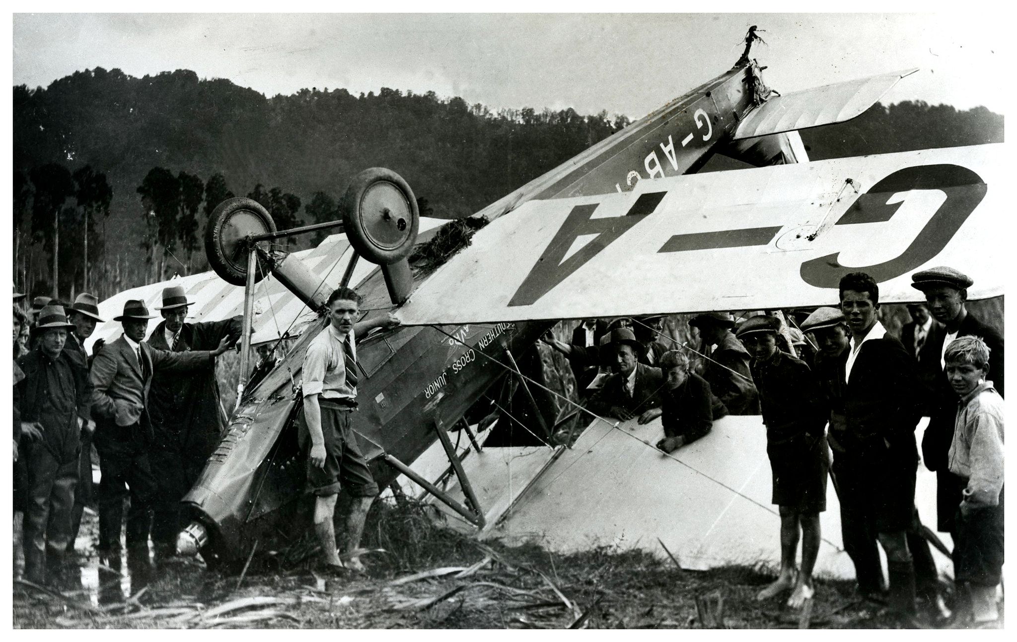 Many people stnading near a biplane that flipped over and crashed .
