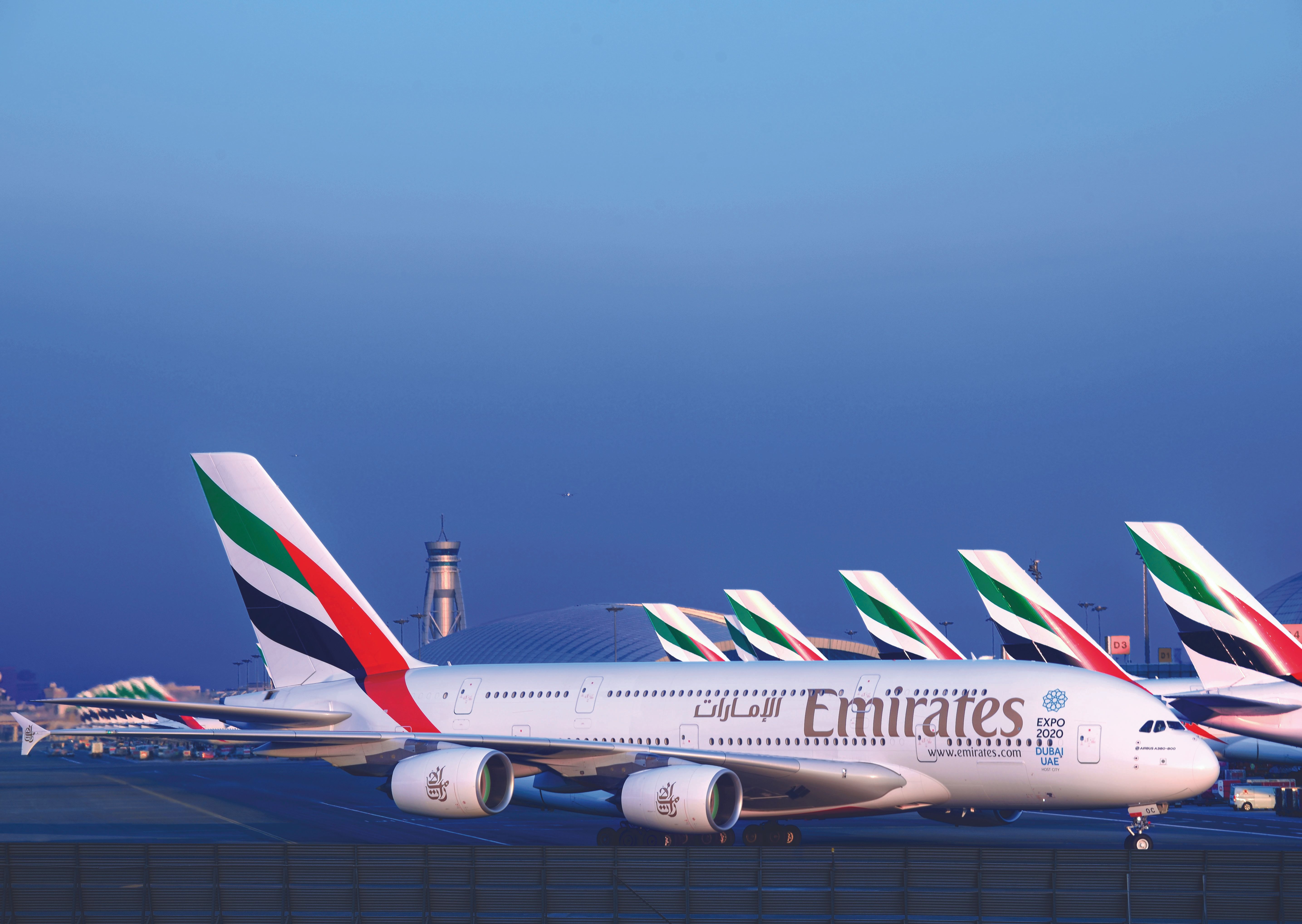 An Emirates Airbus A380 taxis past a line of many other Emirates aircraft.