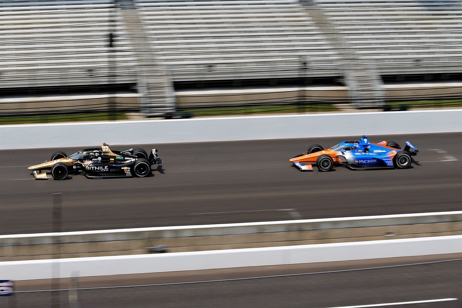 Two race cars speeding on the Indianapolis Motor Speedway track.