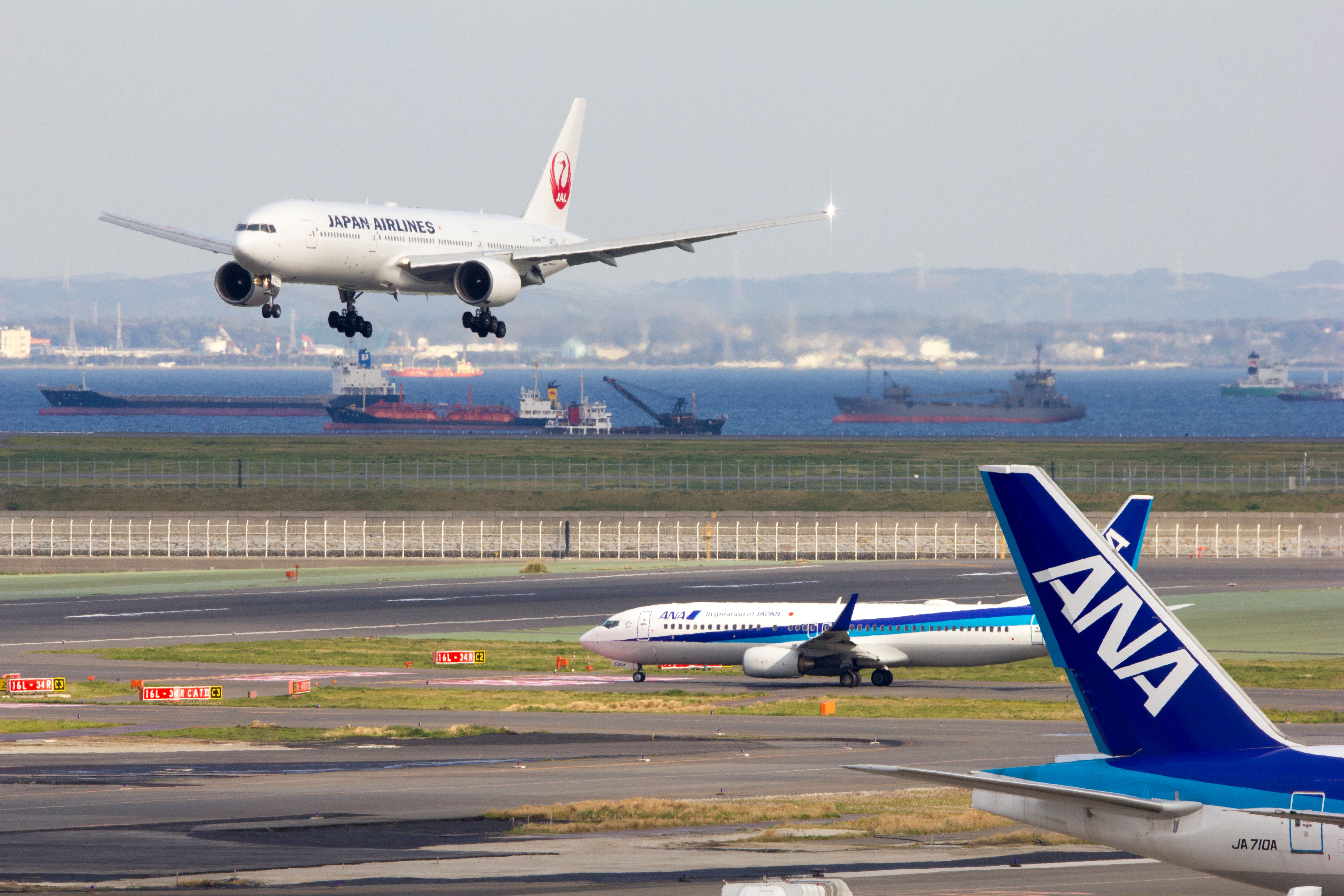 A Japan Airlines Boeing 777 about to land, as an ANA Boeing 737 waits on the taxiway.