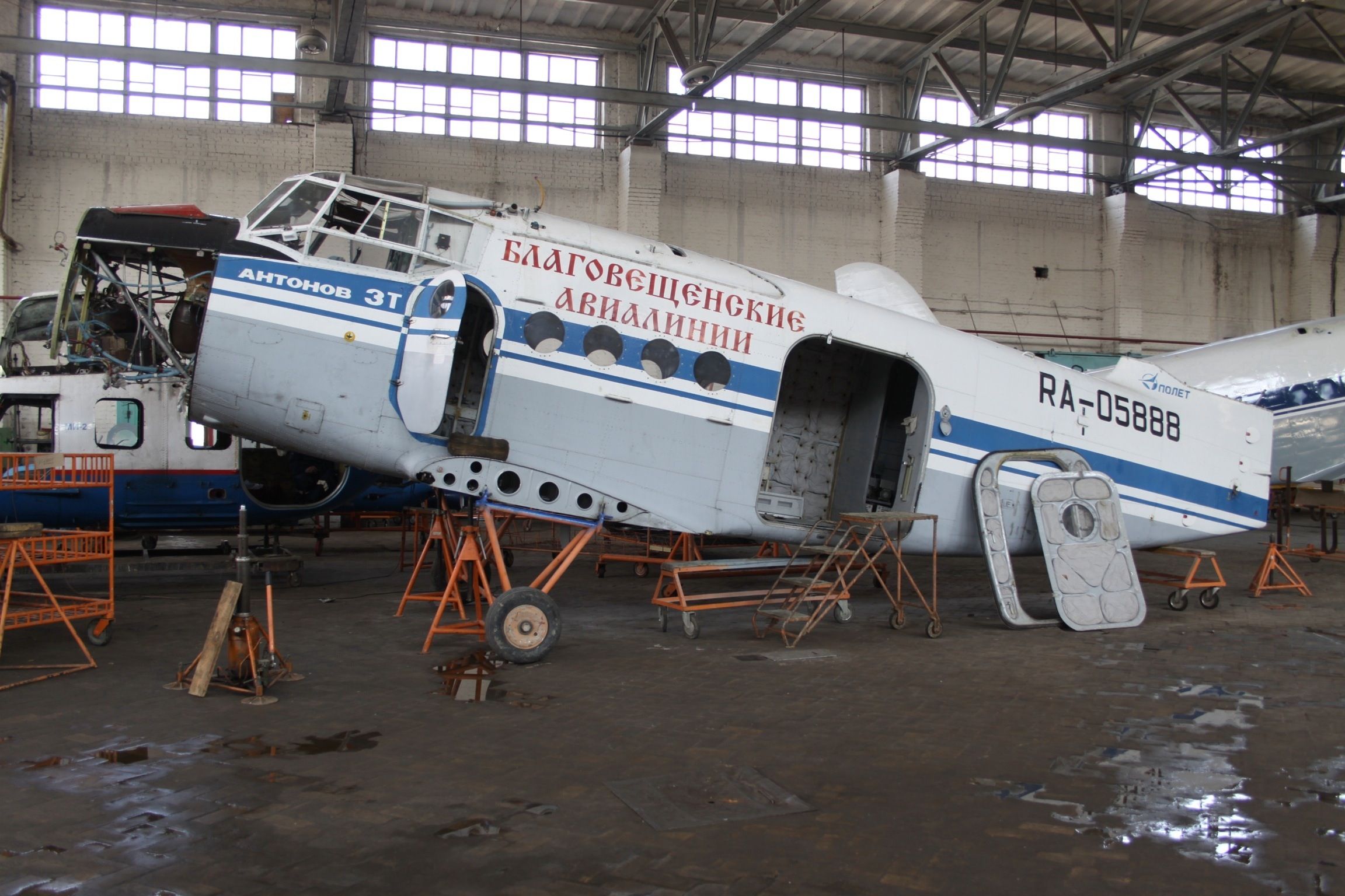 A white and gray transport aircraft with Russian lettering on its side being assembled in a hangar.