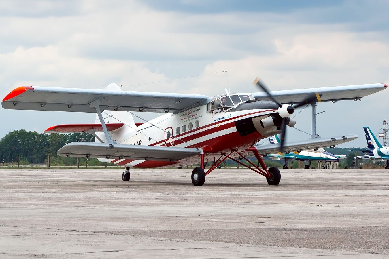 White biplane with red stripes on the bottom half sits on a taxiway.