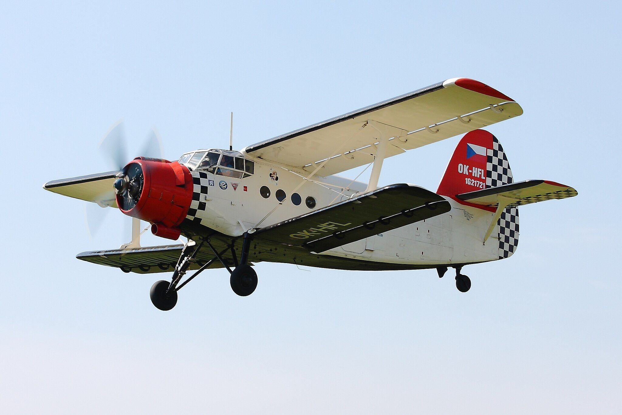 White biplane with red nose and tail flying in blue sky.