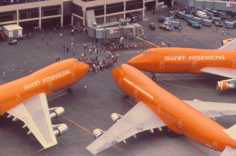 Three Braniff International Boeing 747s near an airport gate. 