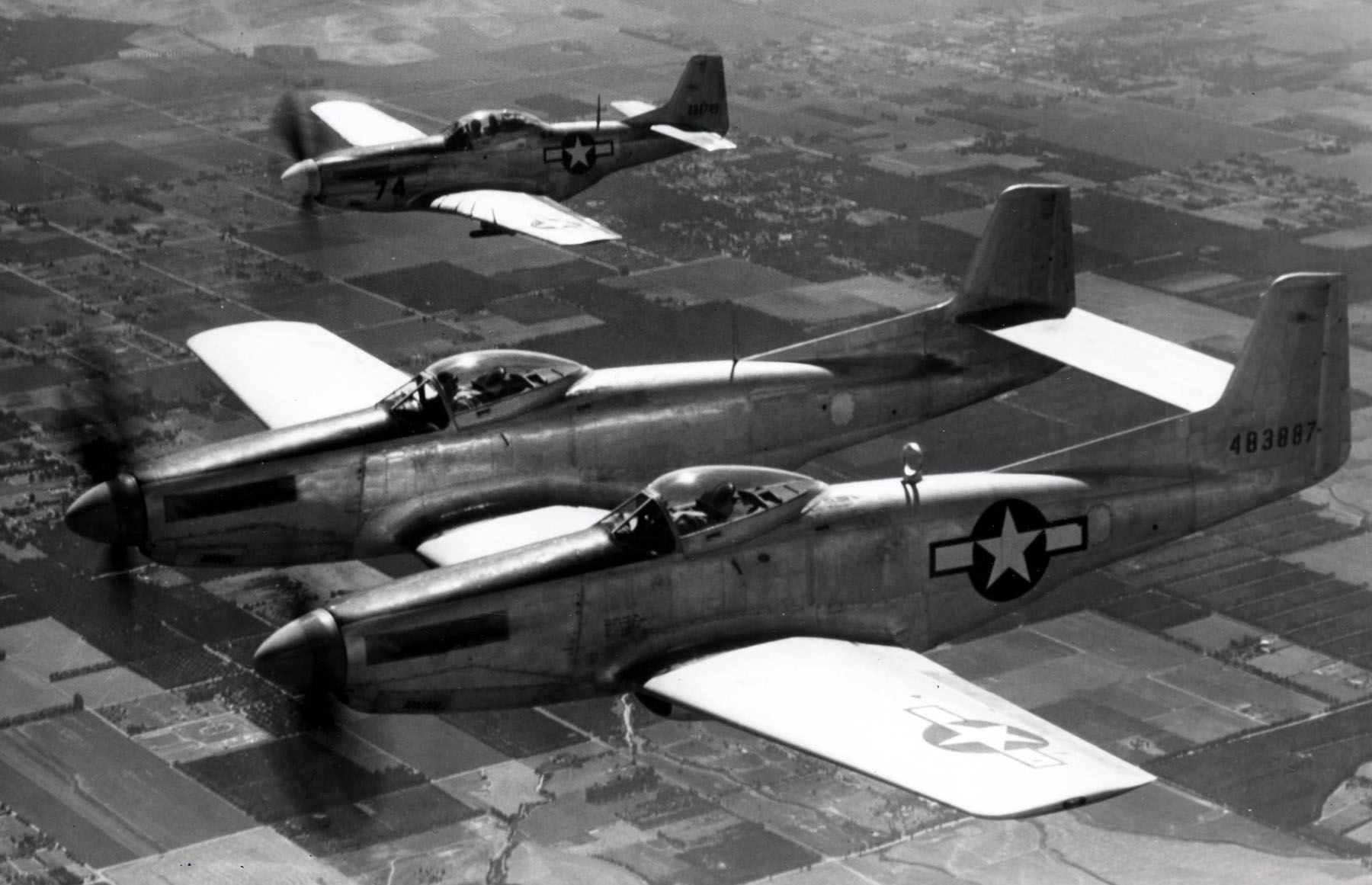 An F-82 and P-51 flying in formation over land.