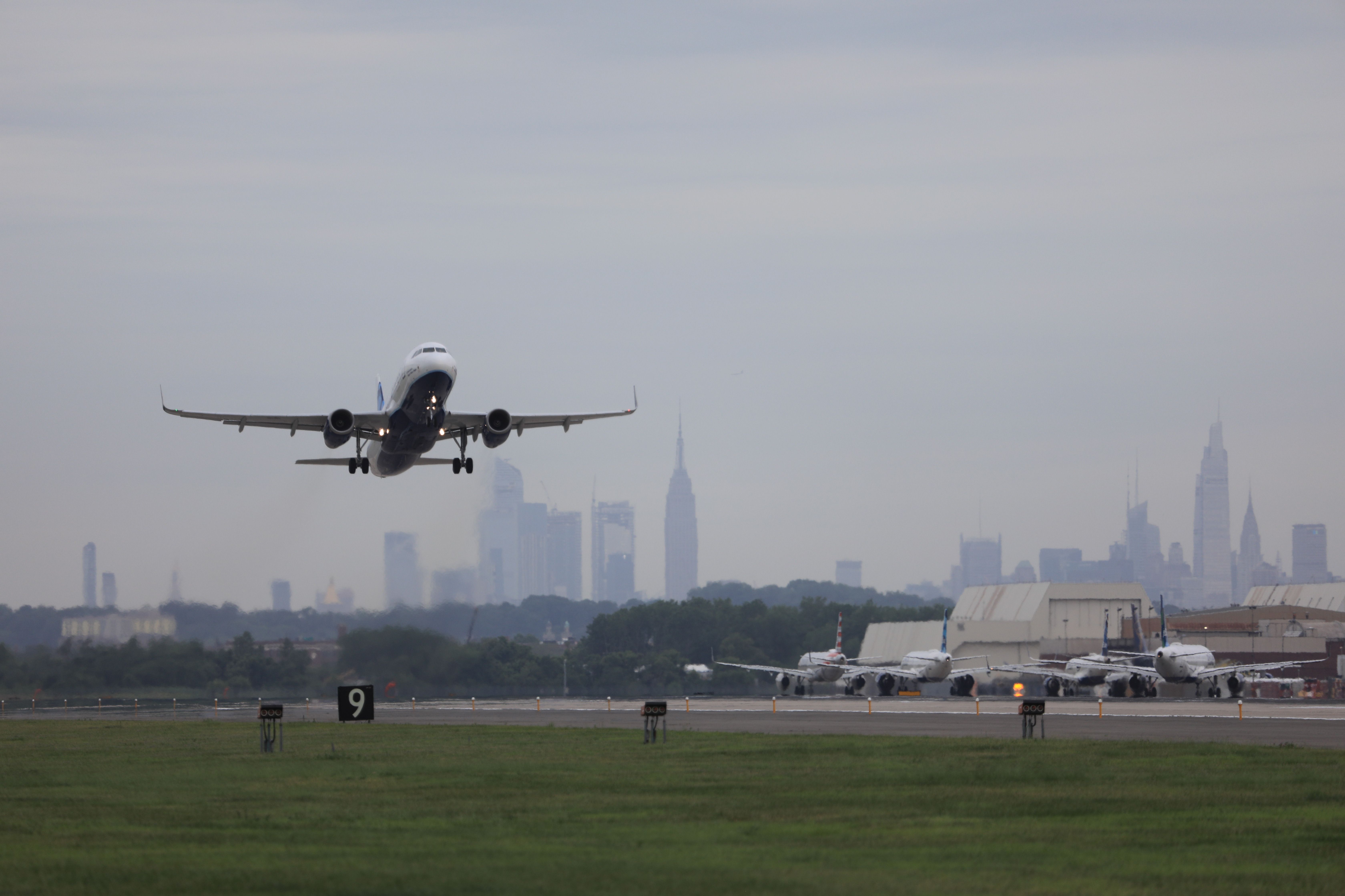 A white jetliner takes off from the runway at JFK airport with the New York City skyline in the backgroundl