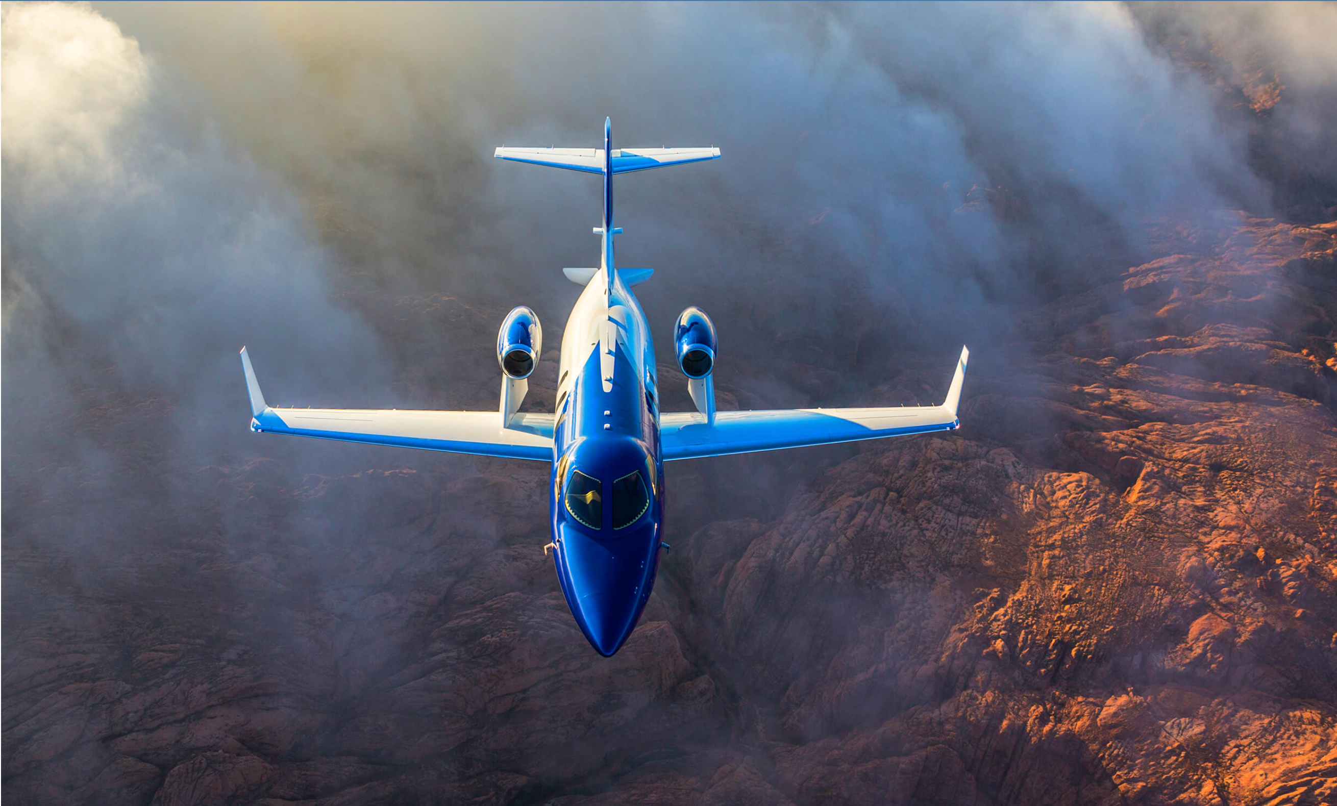 A HondaJet HA-420 flying over mountainous terrain.