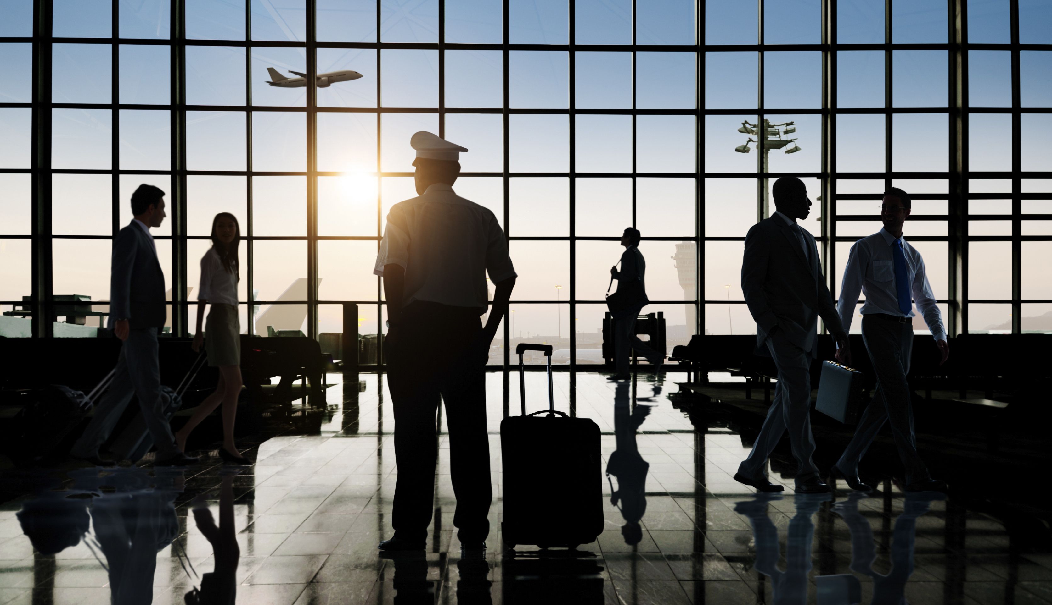 A pilot stands between many passengers at an airport terminal. 