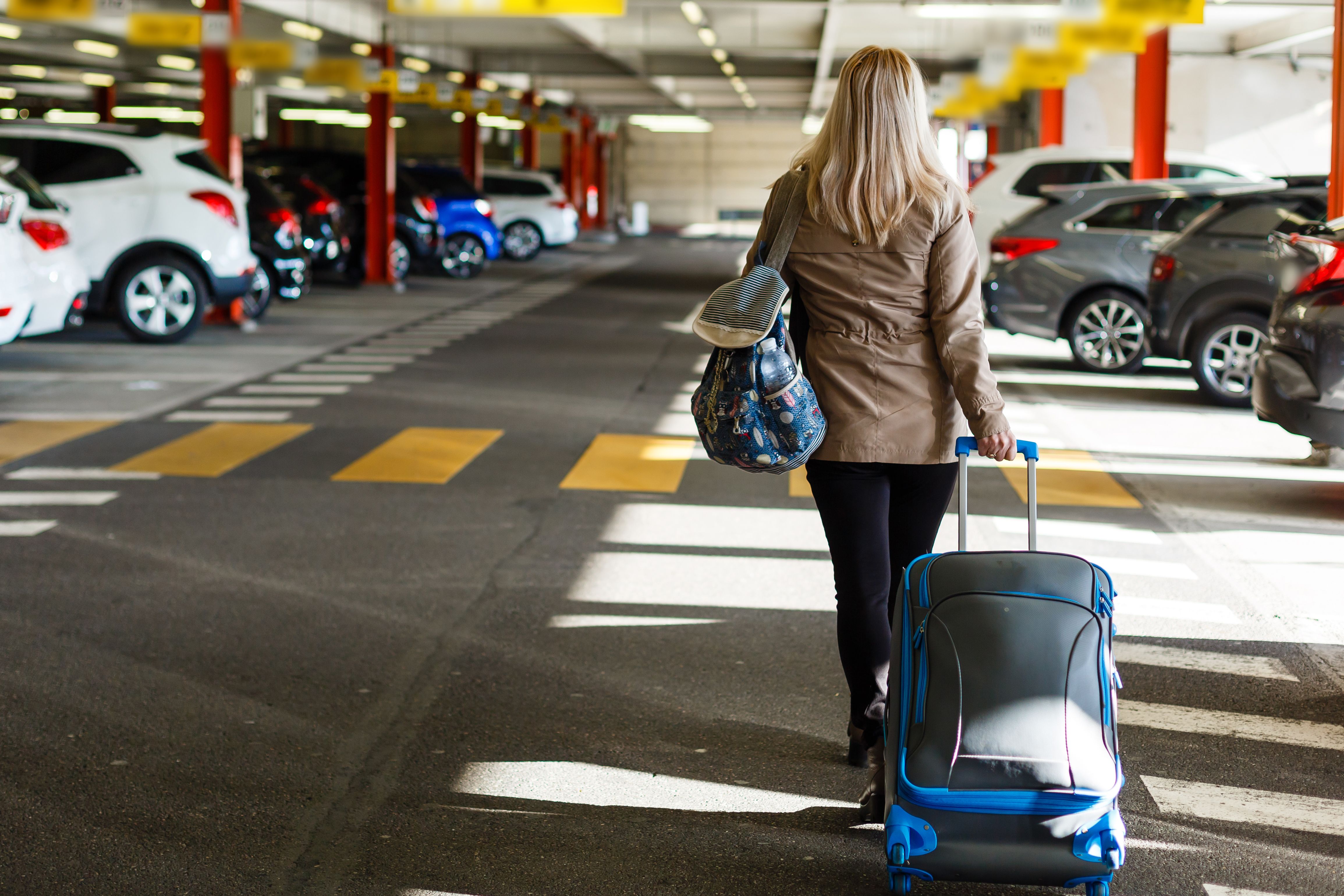 A passenger carrying luggage through an airport car park.