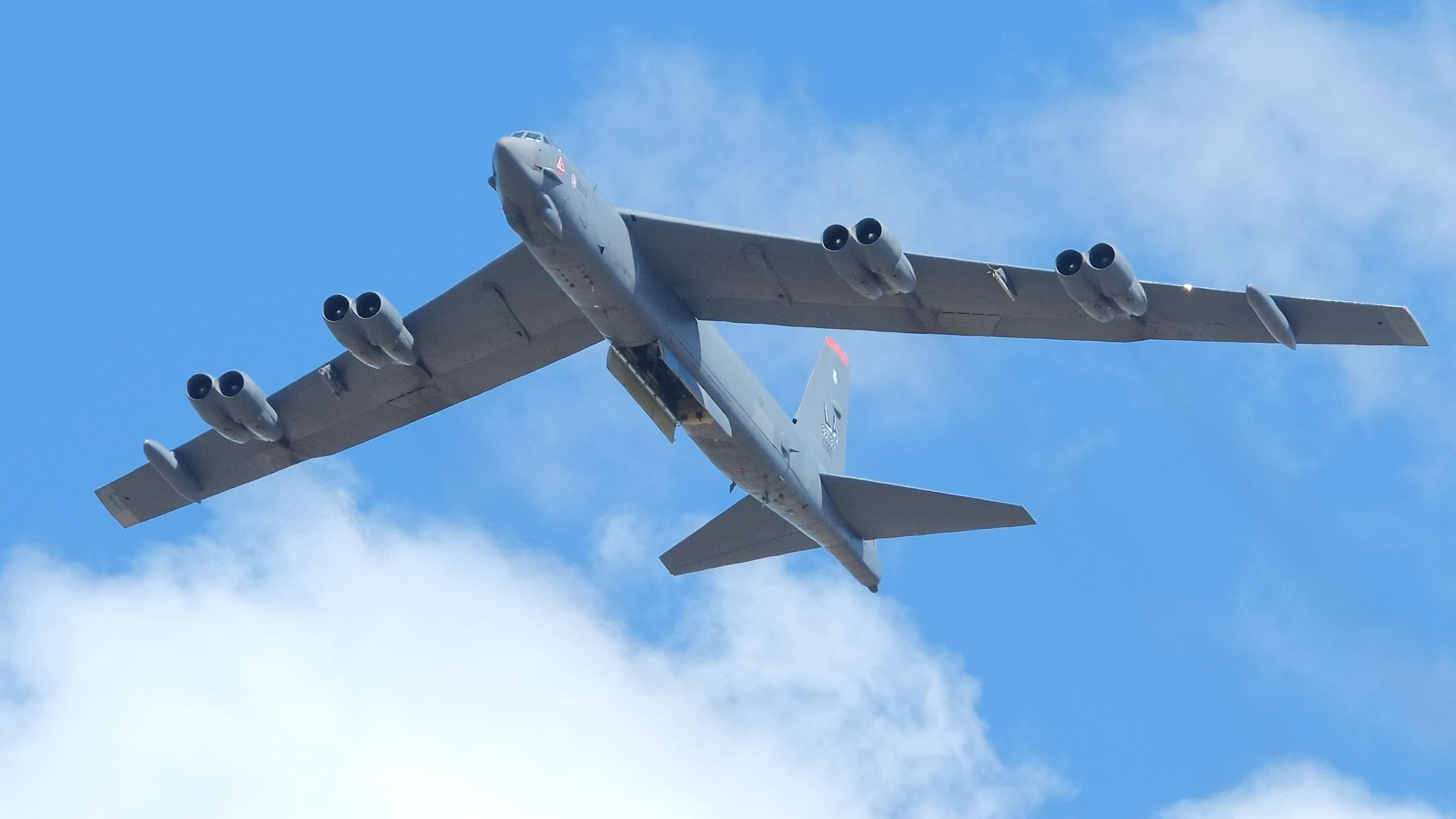 A USAF Boeing B-52 Stratofortress flying overhead with an open bomb bay door.