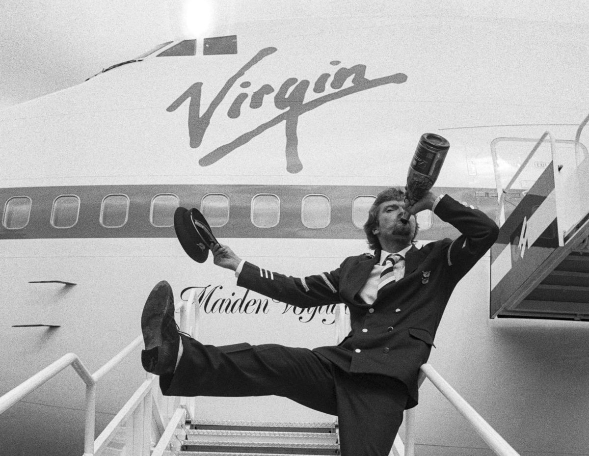 Richard Branson drinking wine from the bottle next to a Virgin Atlantic Boeing 747.