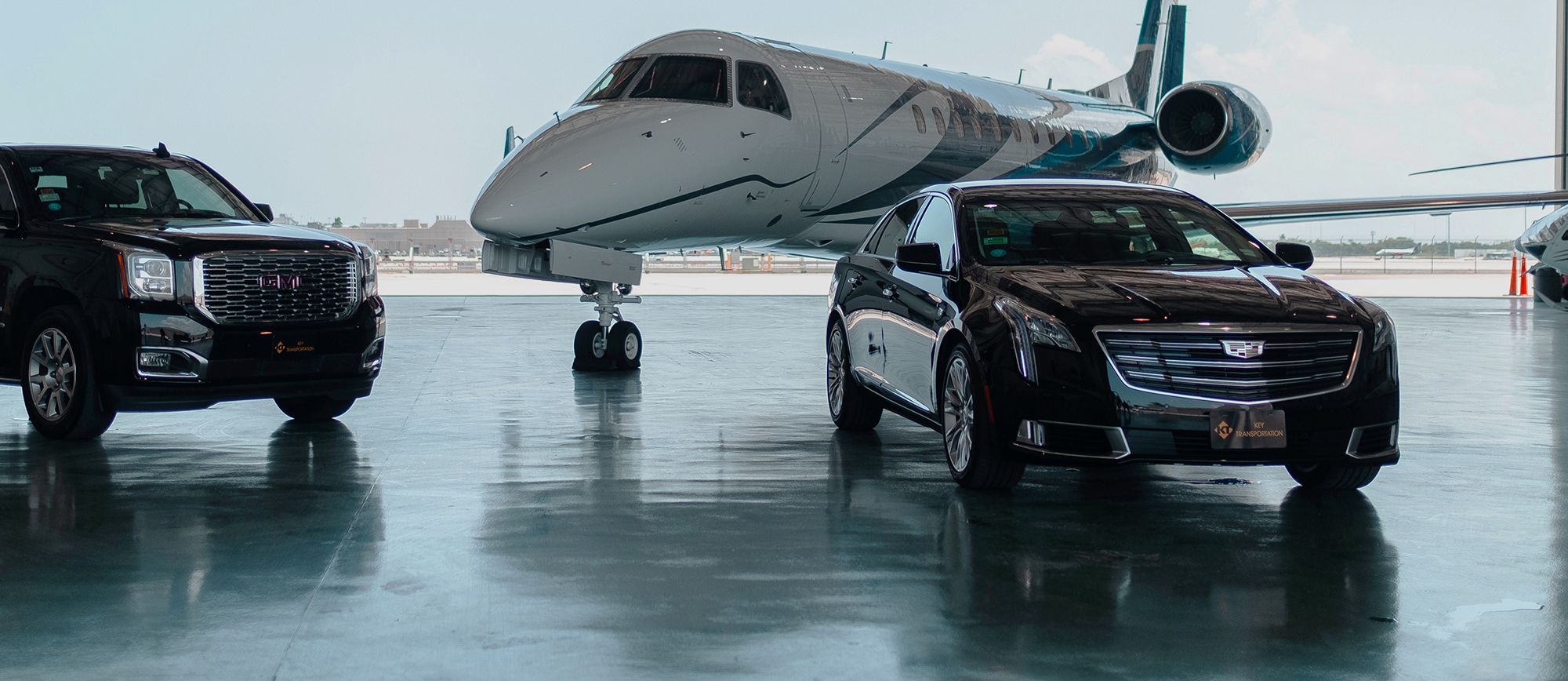 A private jet parked behind two luxury vehicles in a hangar.