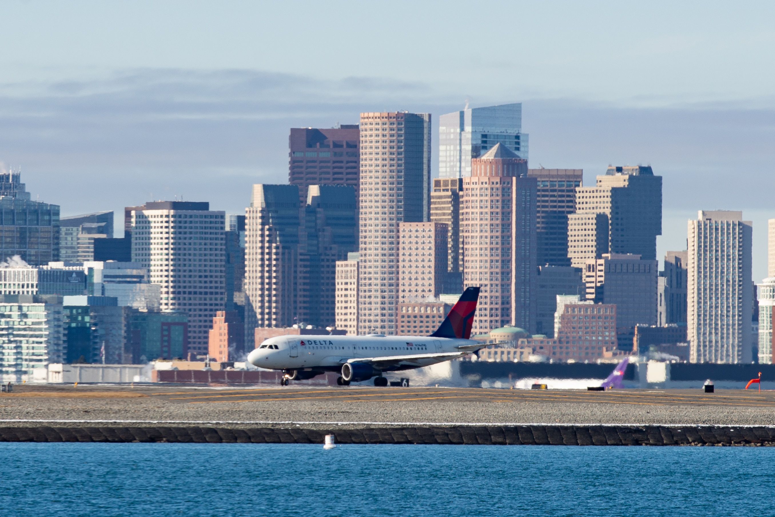 A Delta Air Lines aircraft on a taxiway at Boston Logan Airport with the Boston skyline in the background.