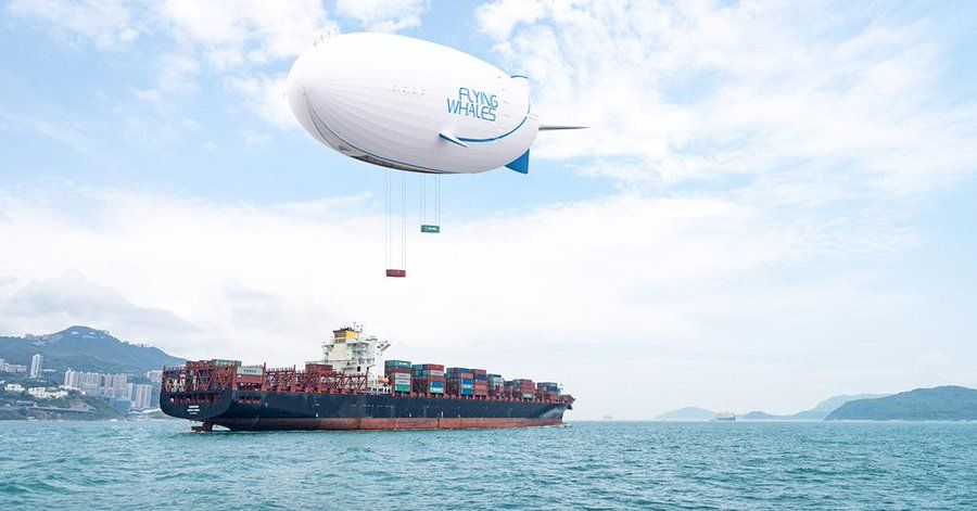A FLYING WHALES airship carrying freight containers flying over water.