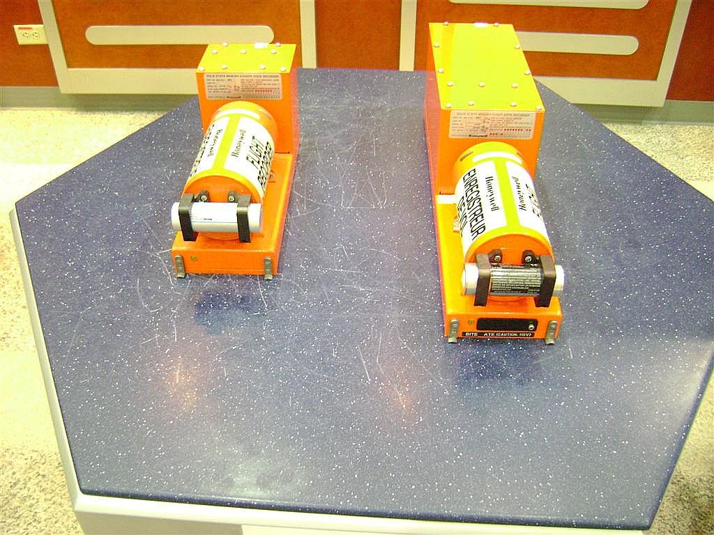 Two  aircraft Flight recorders sitting on a table.