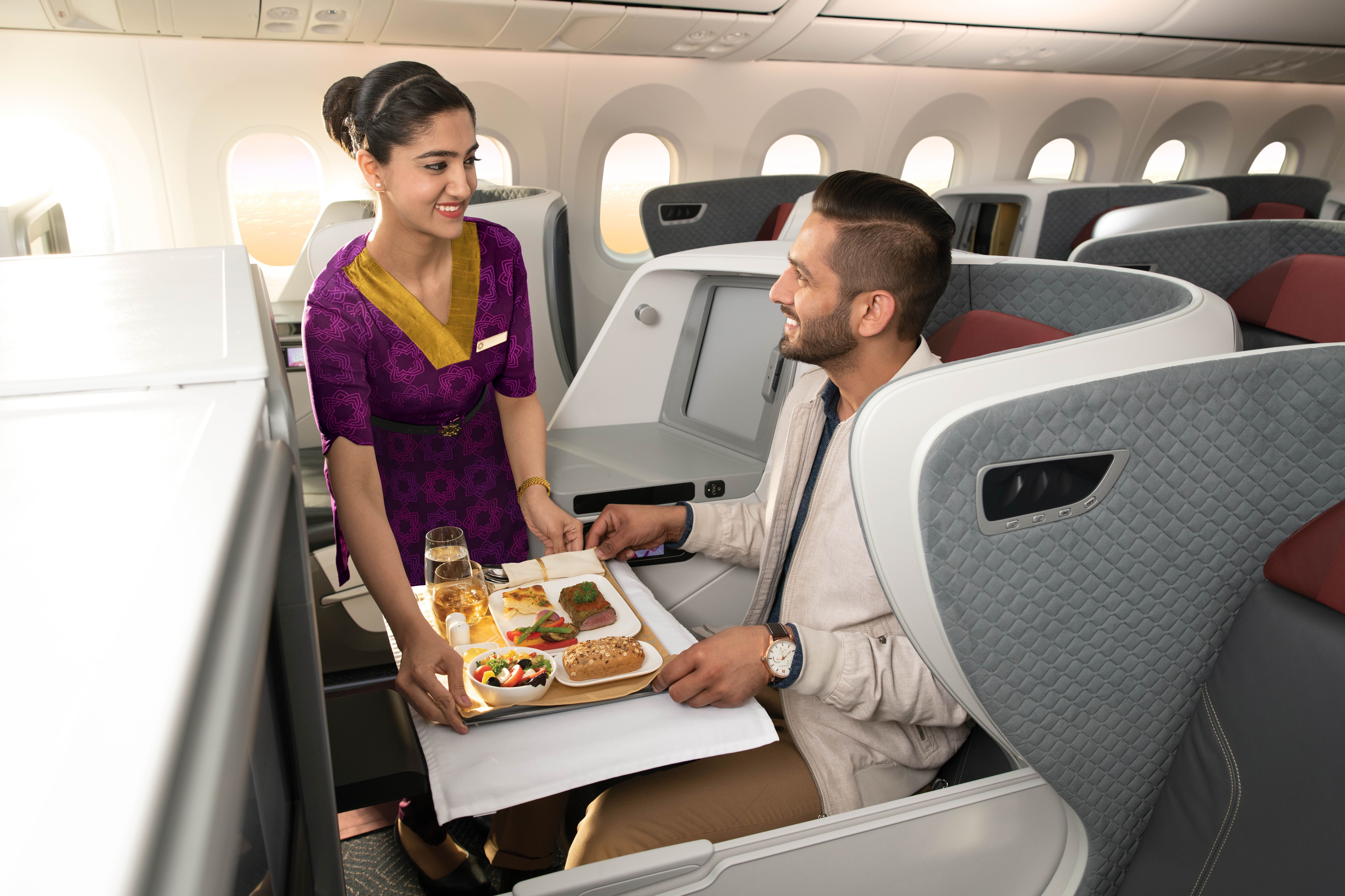 A Vistara flight attendant serving a meal to a passenger in business class.