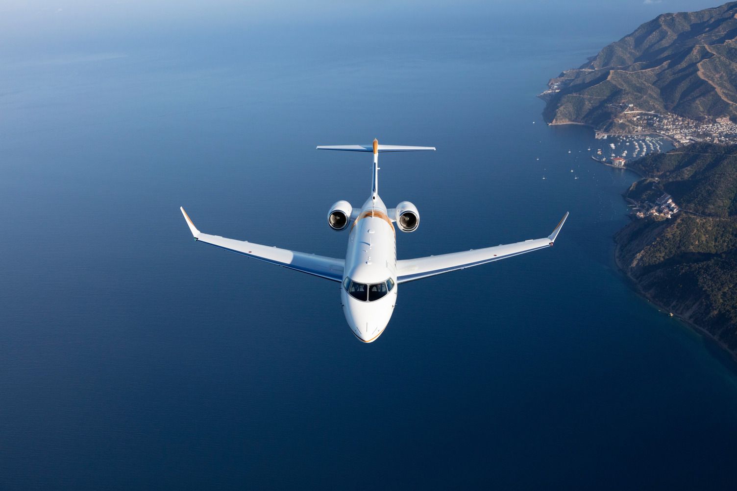 A Bombardier Challenger 3500 flying over water near a marina.